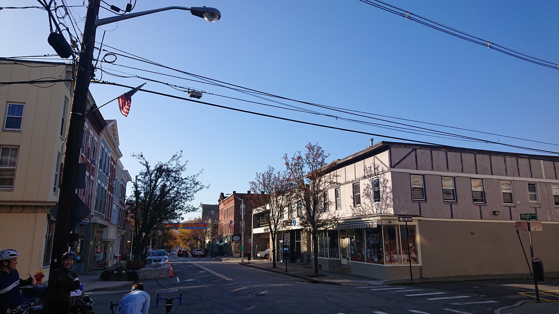Sunny street with historic buildings, power lines, and cyclists.