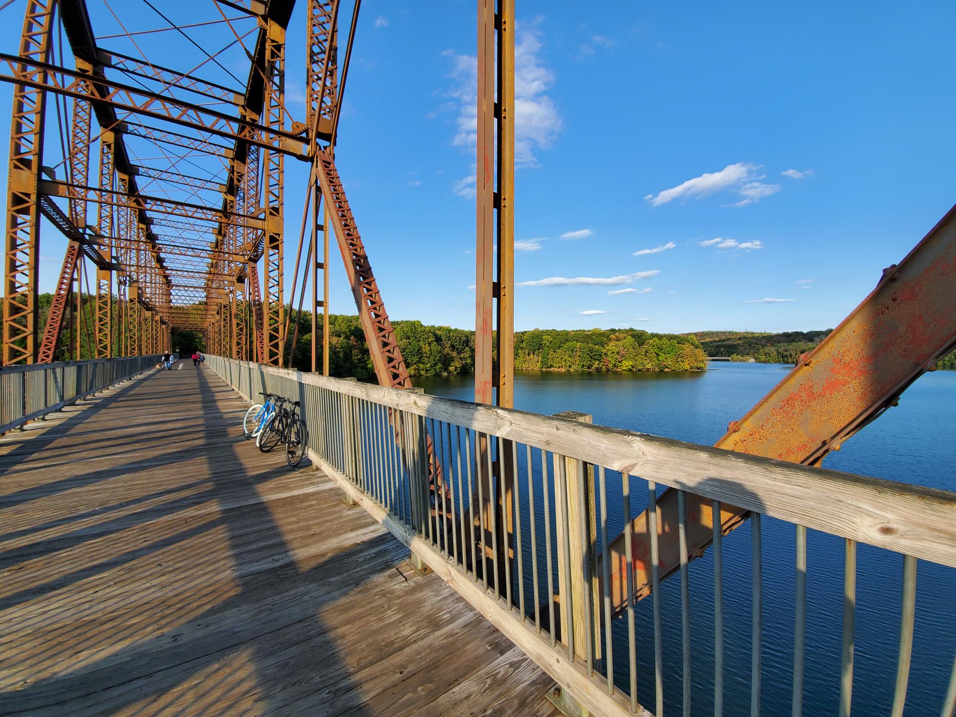 Two bicycles parked on a rusty metal bridge over a sunny lake.