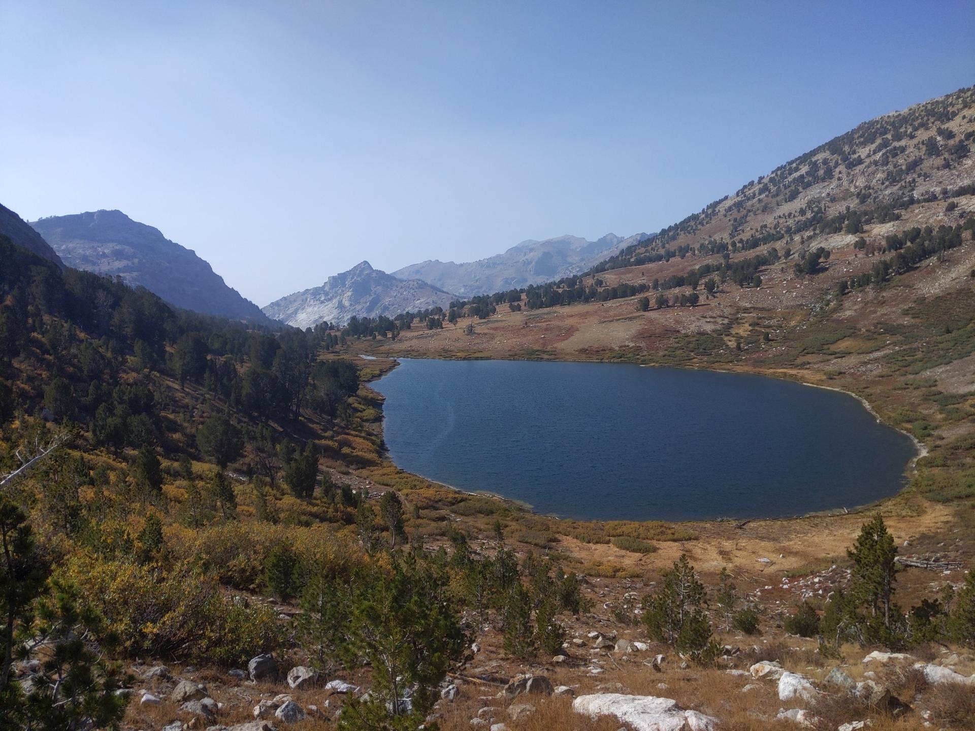 A serene mountain lake surrounded by dry, rocky hillsides on a sunny day.