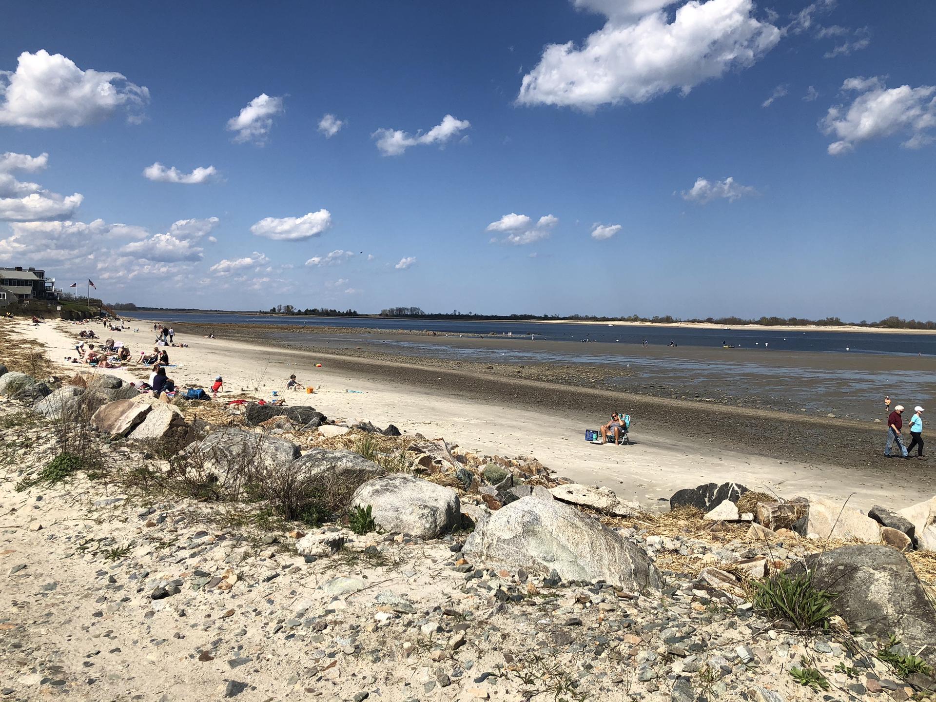 Sandy beach with rocks and people enjoying a sunny day by the water.