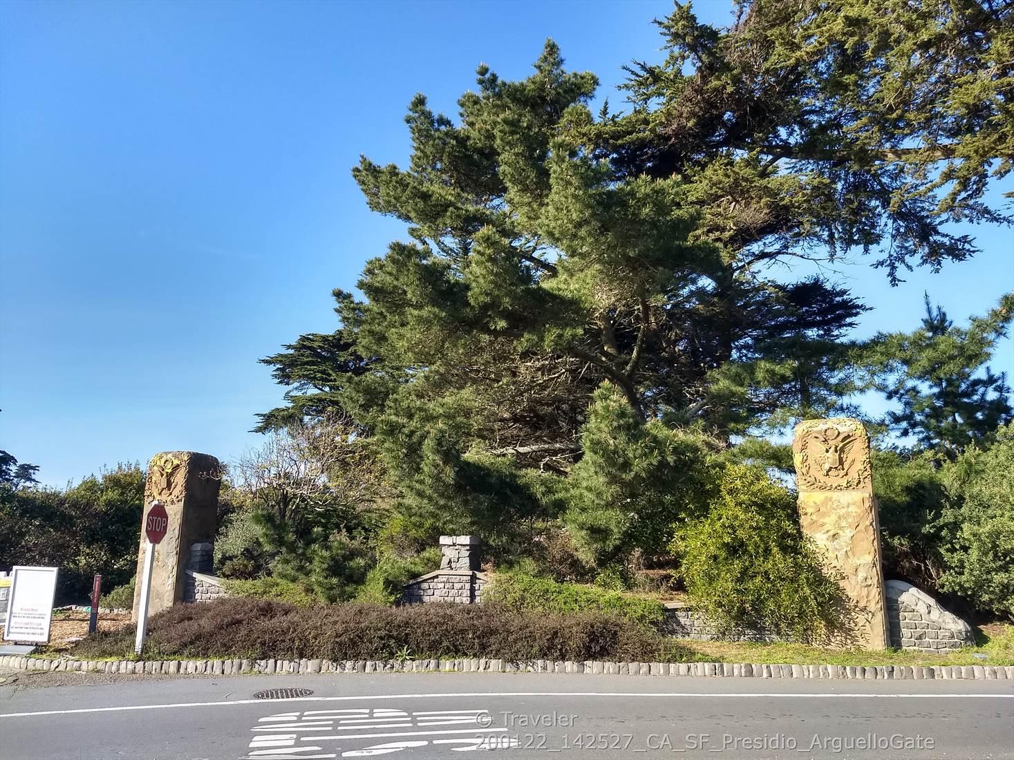 Two ornate stone pillars flank a road next to large evergreen trees.