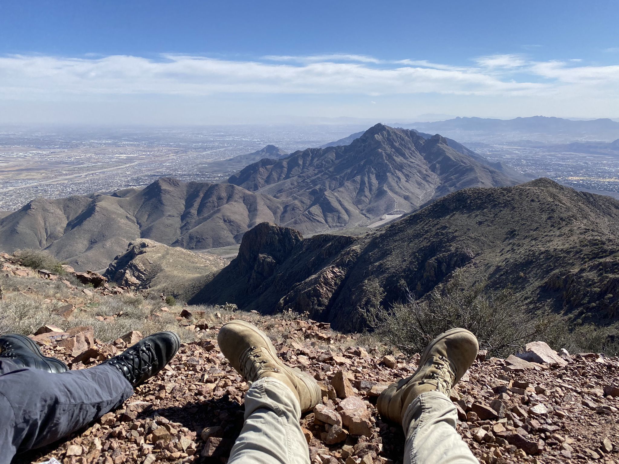 Two people's legs and boots resting on a rocky peak overlooking a city. - North Franklin Peak Trail