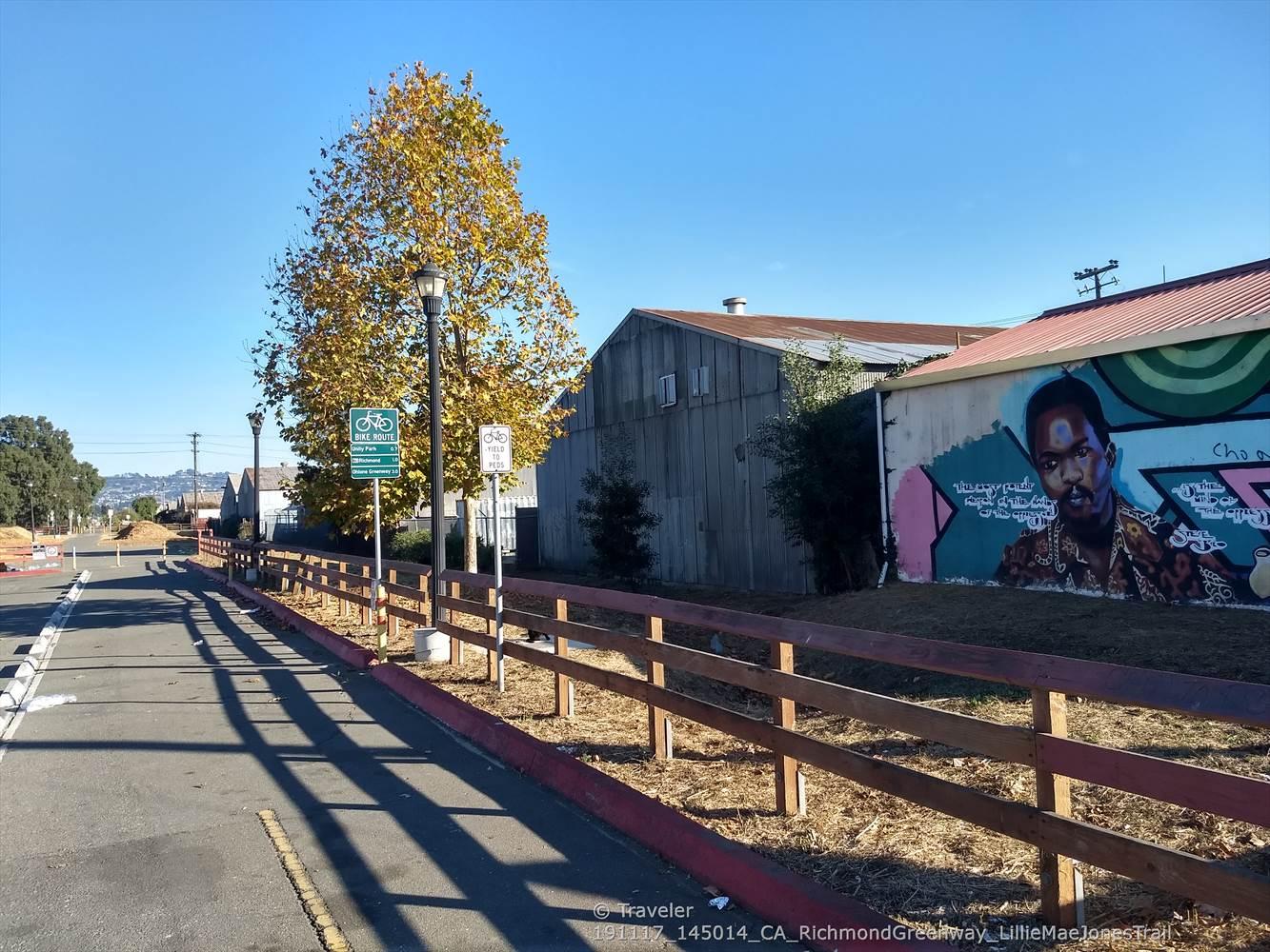 A paved path with a wooden fence next to buildings and a colorful mural.