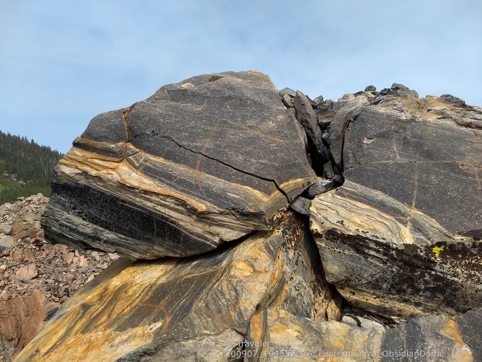 Close-up of a large, cracked rock with distinct black, yellow, and brown layers.