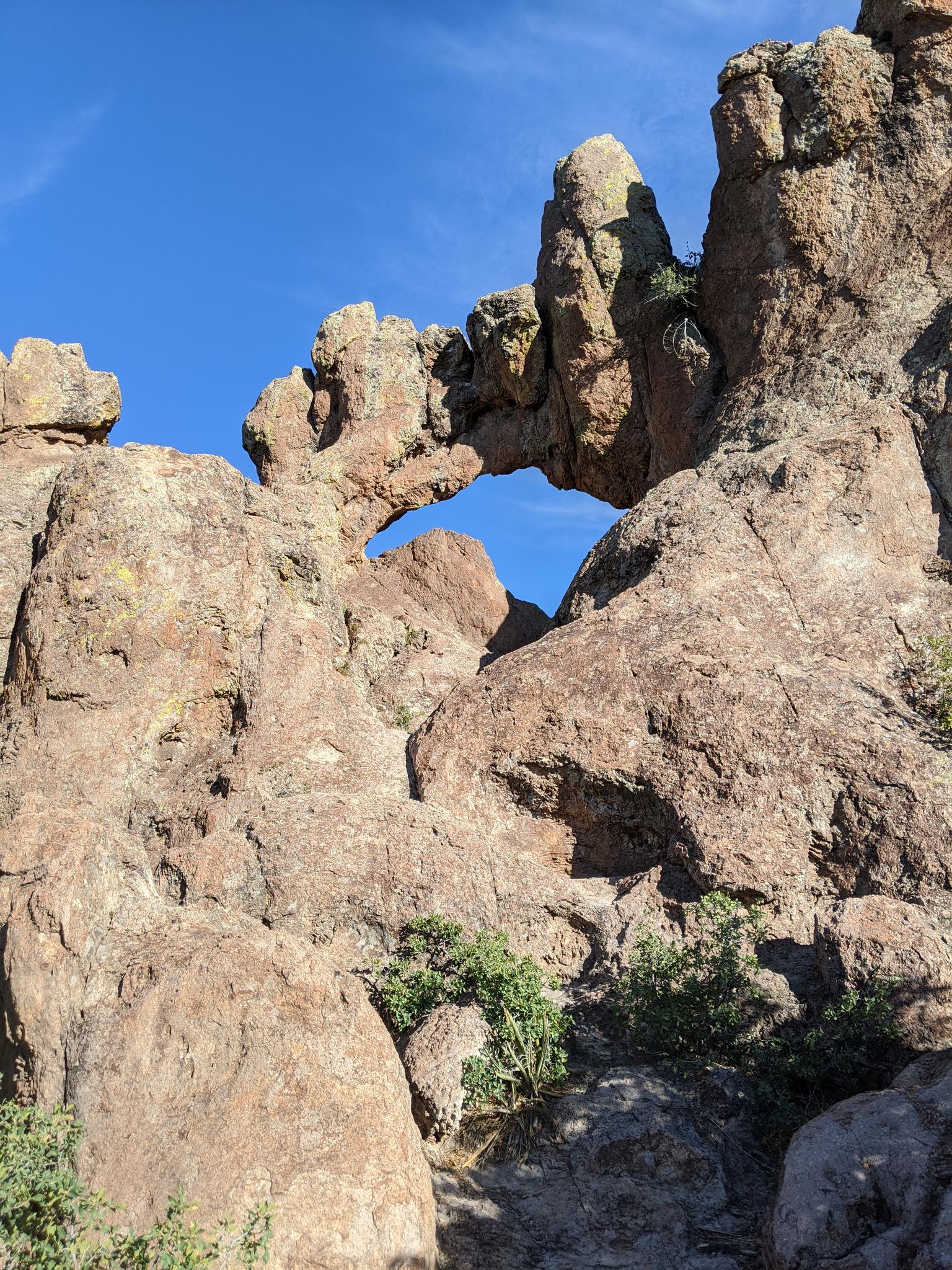 A natural rock arch formation stands against a clear blue sky.