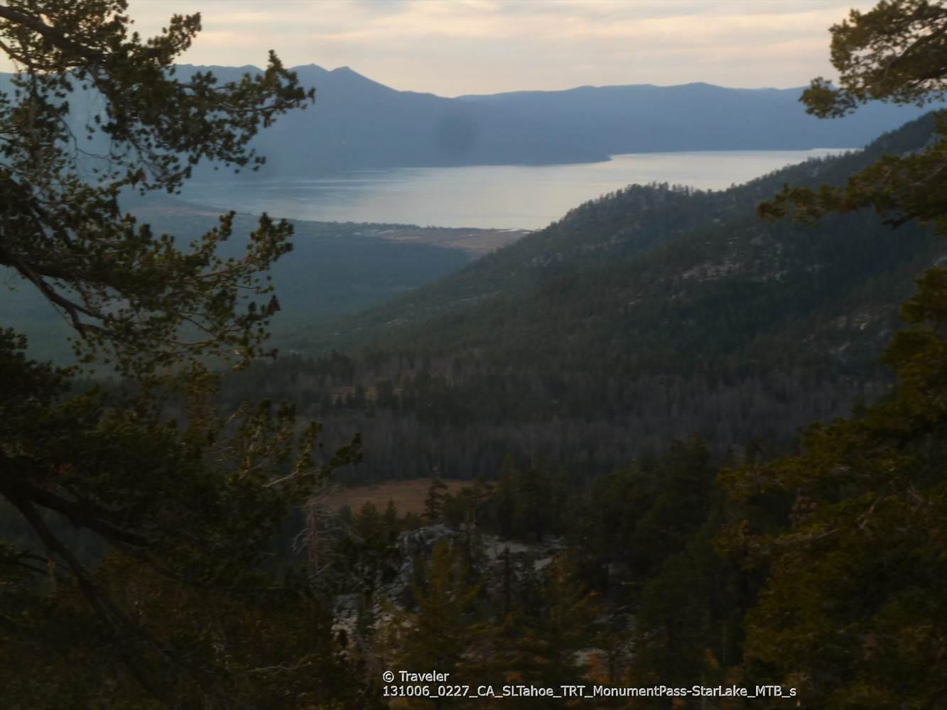 Dark, moody lake view nestled between forested mountains under a twilight sky.