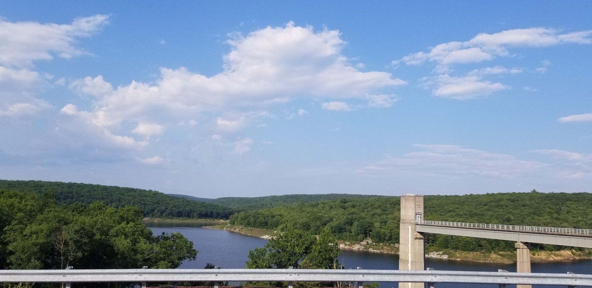 Expansive lake and green forests under a bright blue sky with a concrete structure. - White Haven to Frances Walter Dam and Reservoir loop via the D&L Trail
