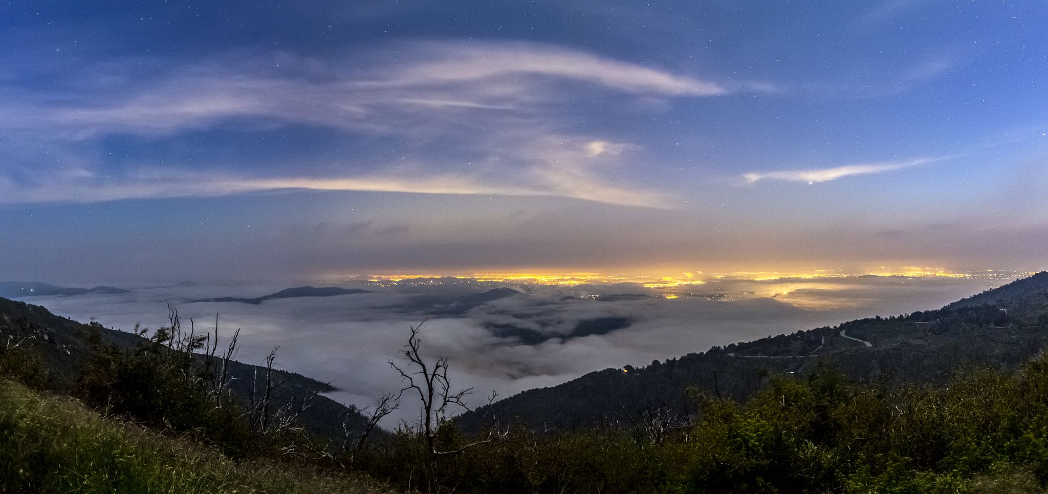 Panoramic mountain view at twilight with glowing city lights under a cloudy sky. - Palomar Mountain – Palomar East Grade loop from Funner