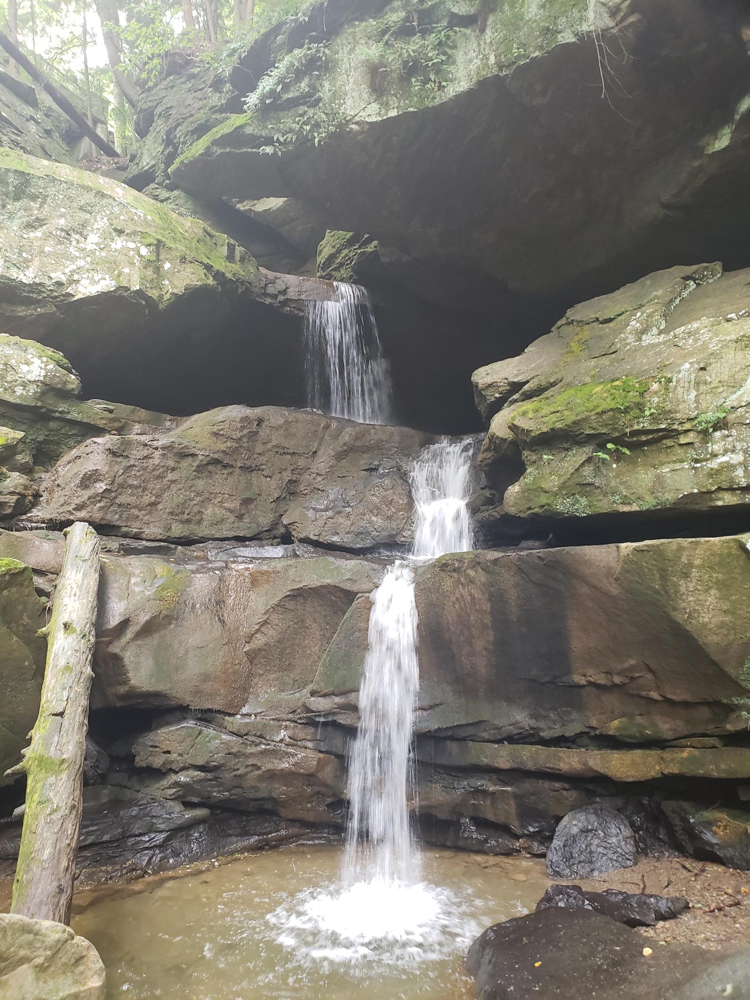 A multi-tiered waterfall cascades over mossy rocks into a small pool.