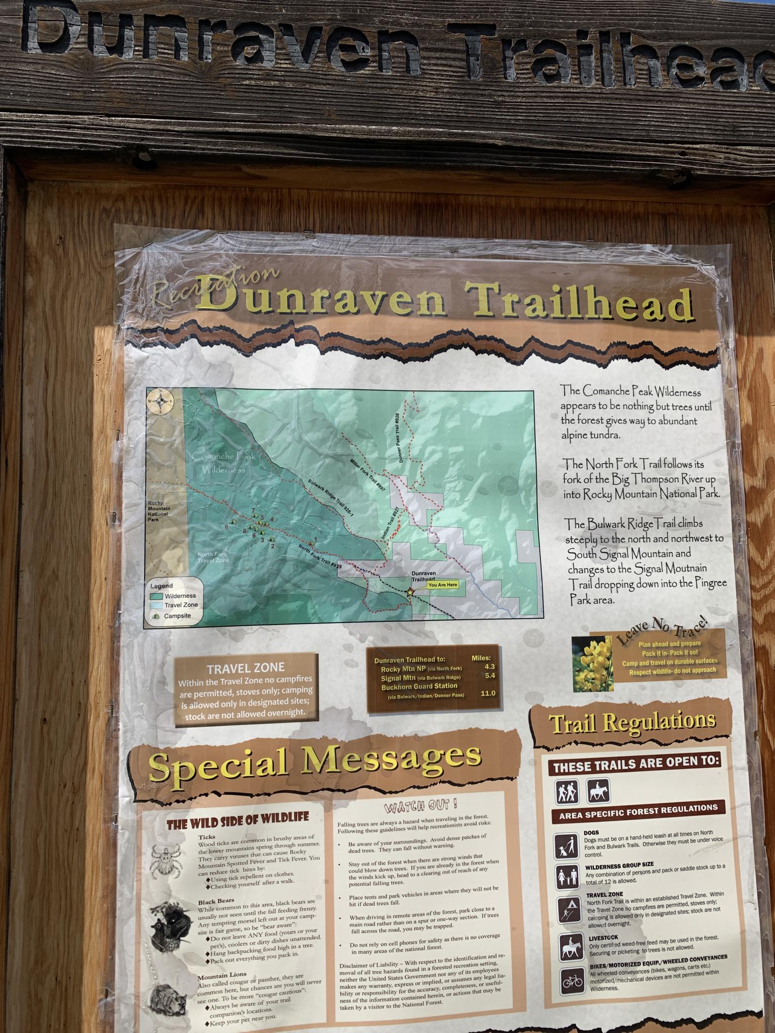 A wooden trailhead sign with a map and information in bright outdoor light.