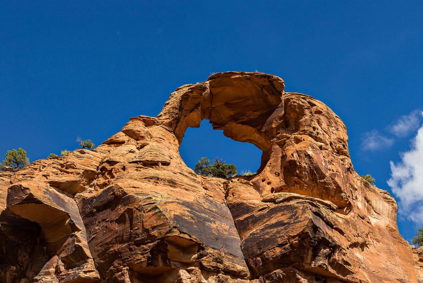 A large, reddish-brown natural rock arch against a vibrant blue sky.