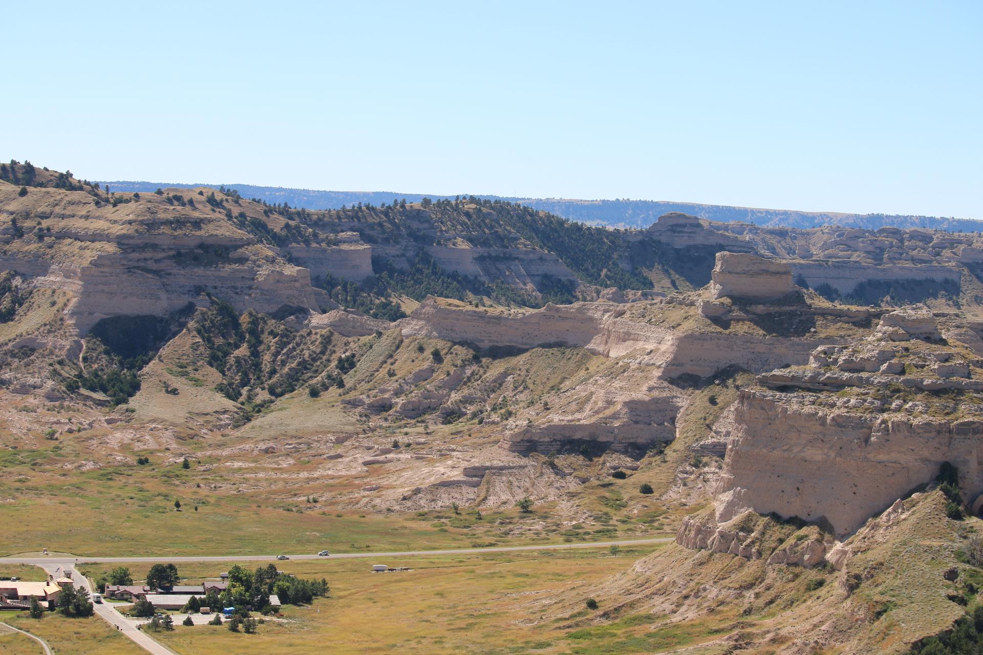 Wide valley with layered cliffs, distant hills, and a small settlement.