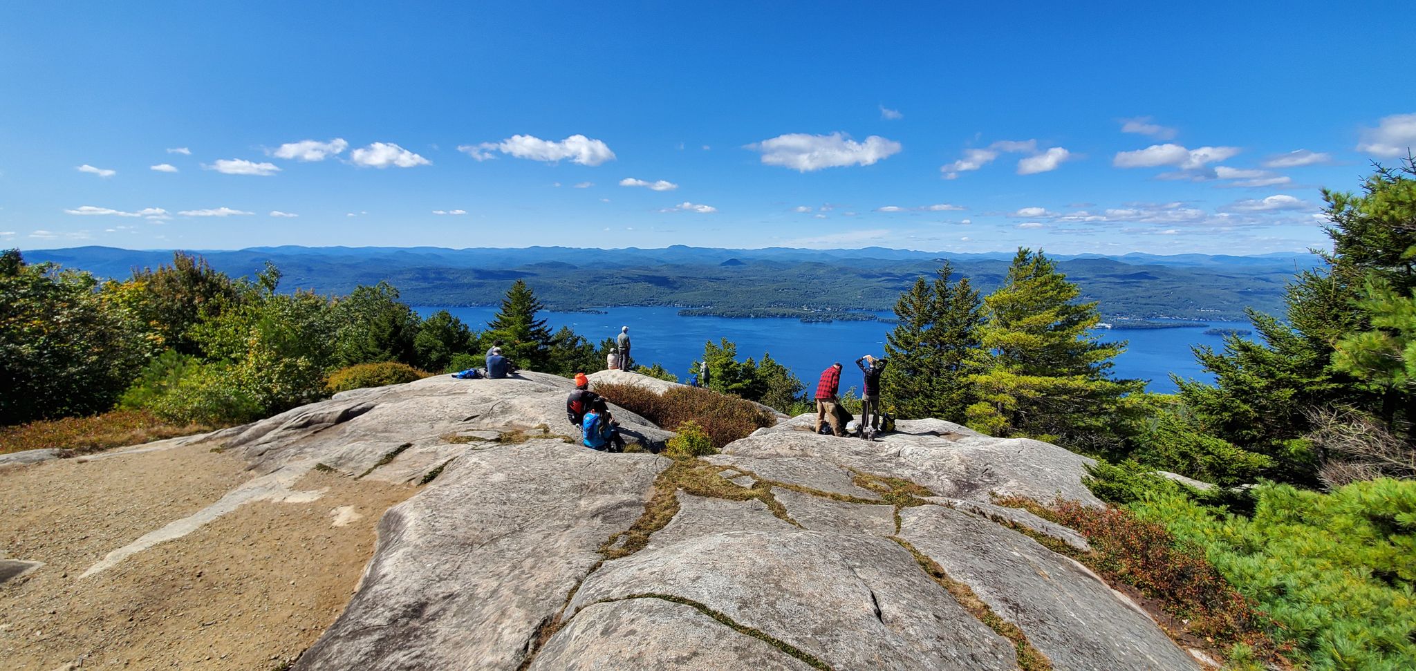 Hikers on a rocky summit overlooking a vast lake under a clear blue sky. - Buck Mt from Pilot Knob Trail