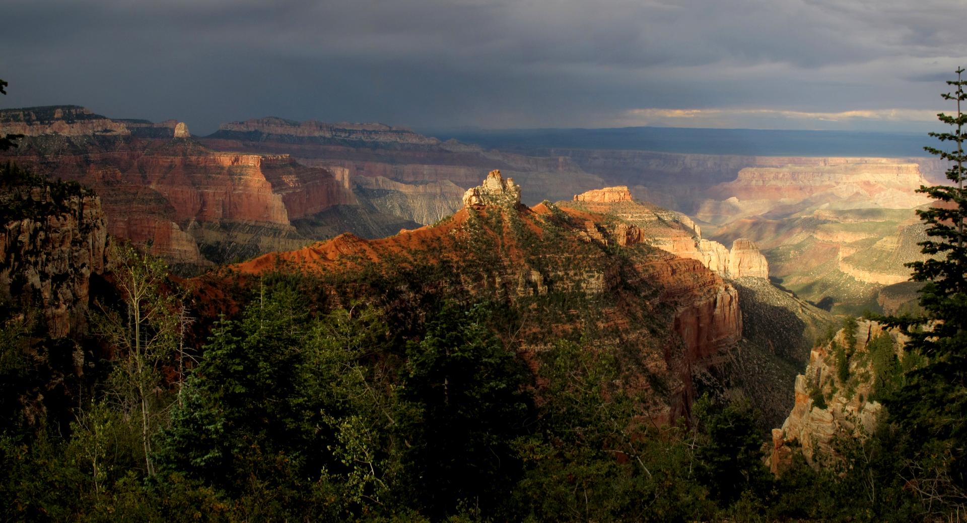 Dramatic canyon landscape with sunbeams illuminating rock formations under dark clouds.