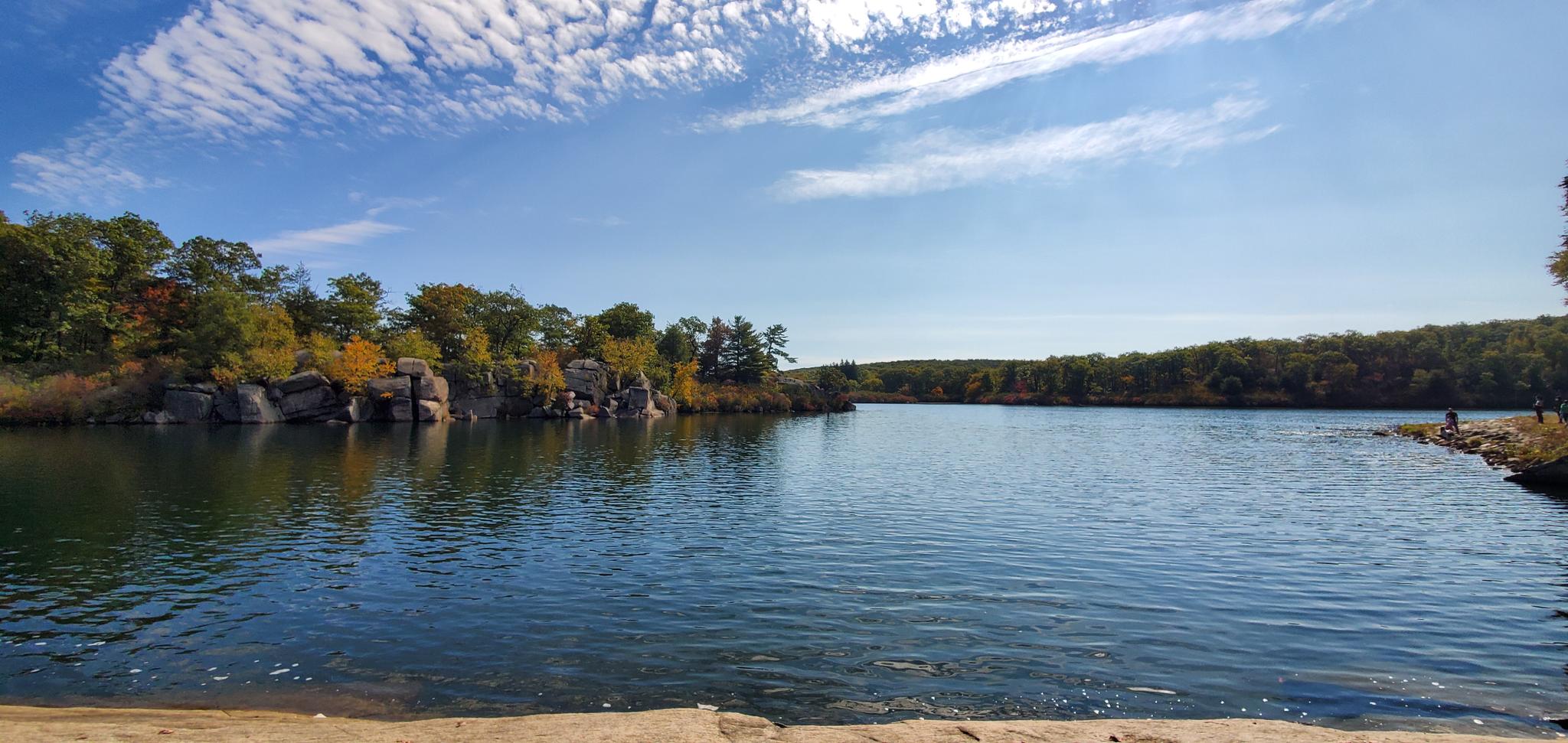 Vibrant lake scene with rocky shores, autumn trees, and a bright blue sky.