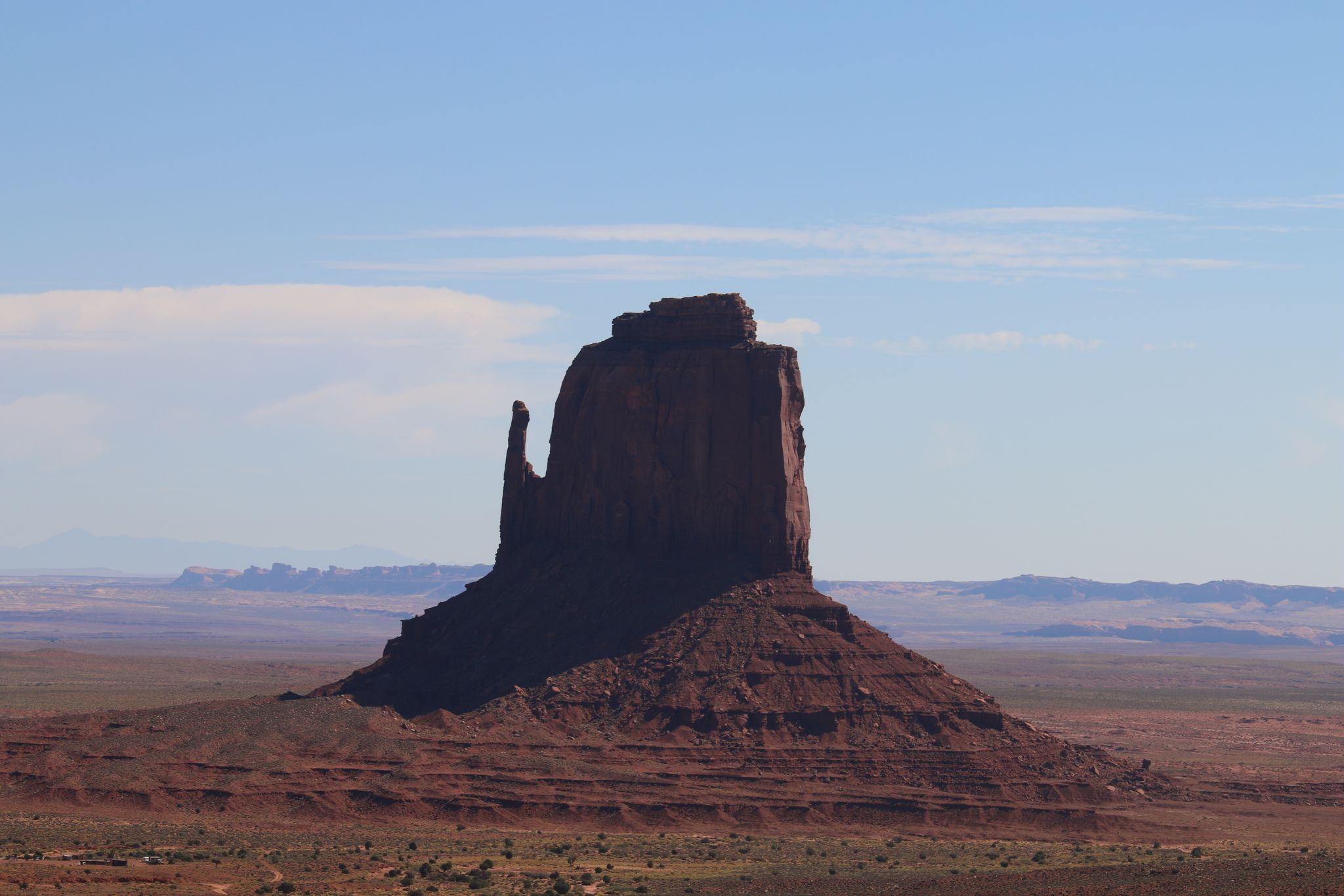 Distant red rock formation silhouetted against a light blue sky in a vast desert. - Wildcat Trail