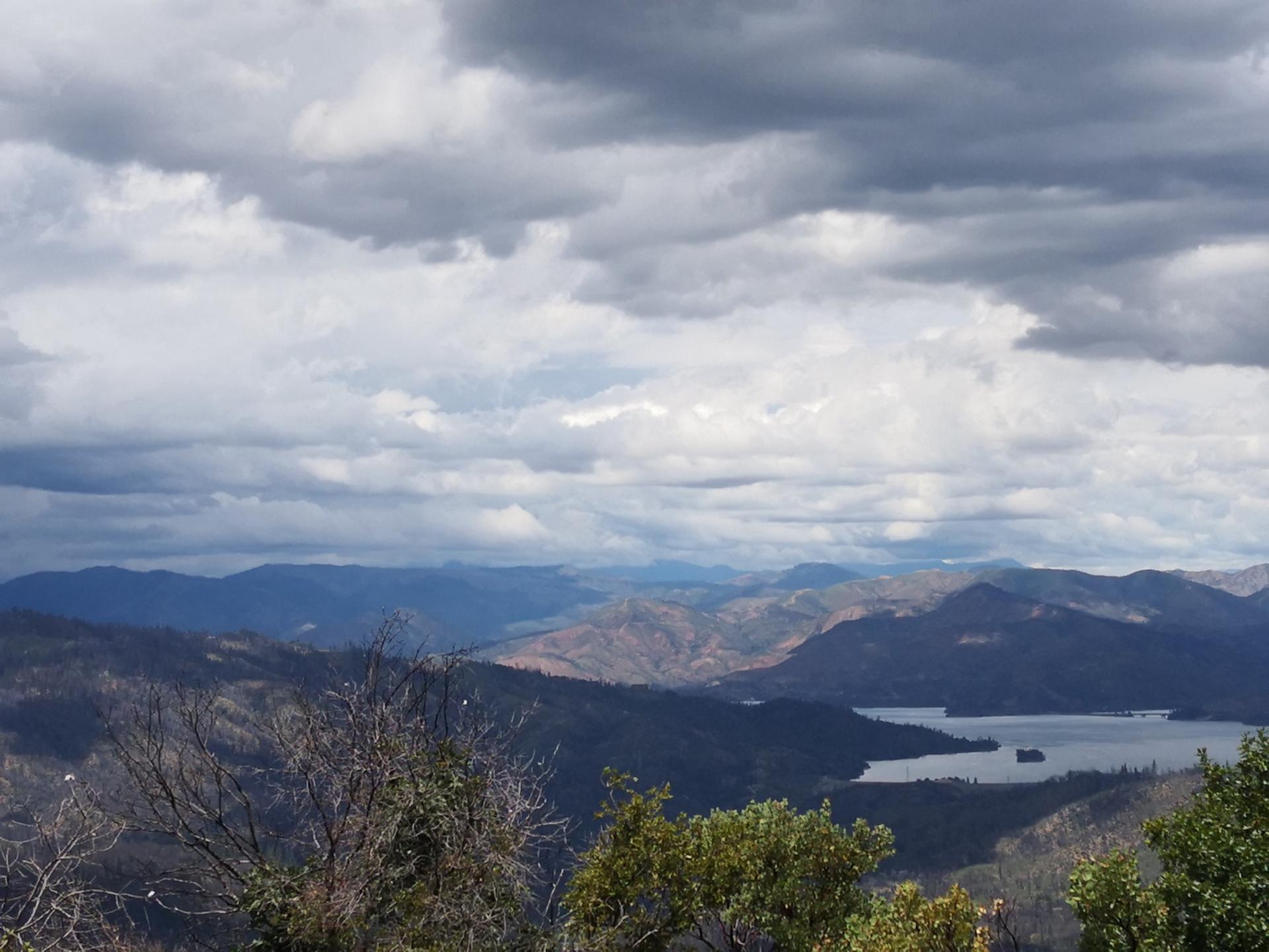Expansive view of a lake nestled among rolling mountains under a cloudy sky.