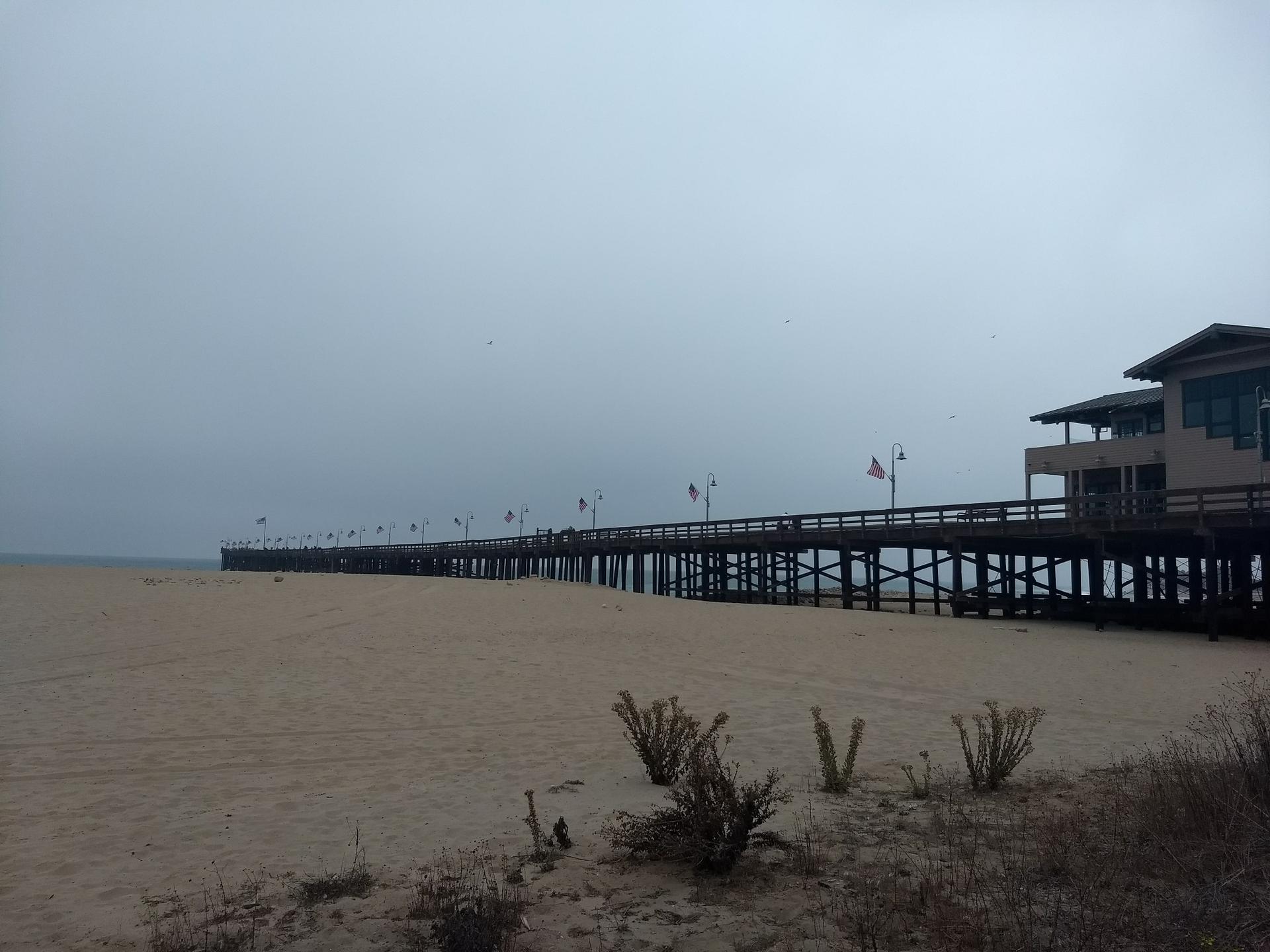 Long wooden pier over a wide sandy beach under a gray, overcast sky.