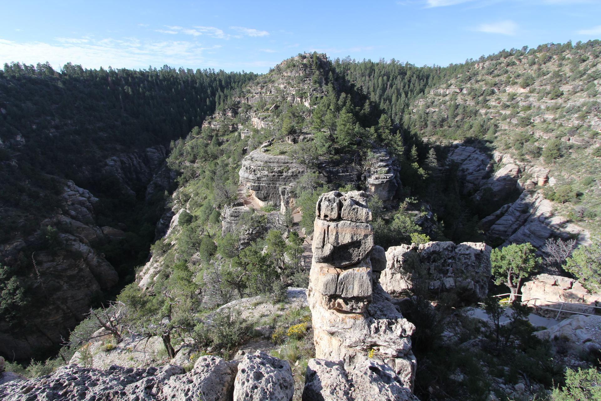 Unique stacked rock formations overlook a forested canyon on a bright day.