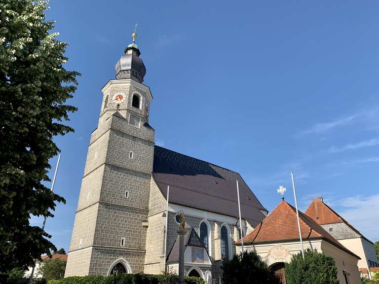Gereja St. Mariä Himmelfahrt di Feichten an der Alz terlihat dari kejauhan, dikelilingi ladang hijau dan langit biru.