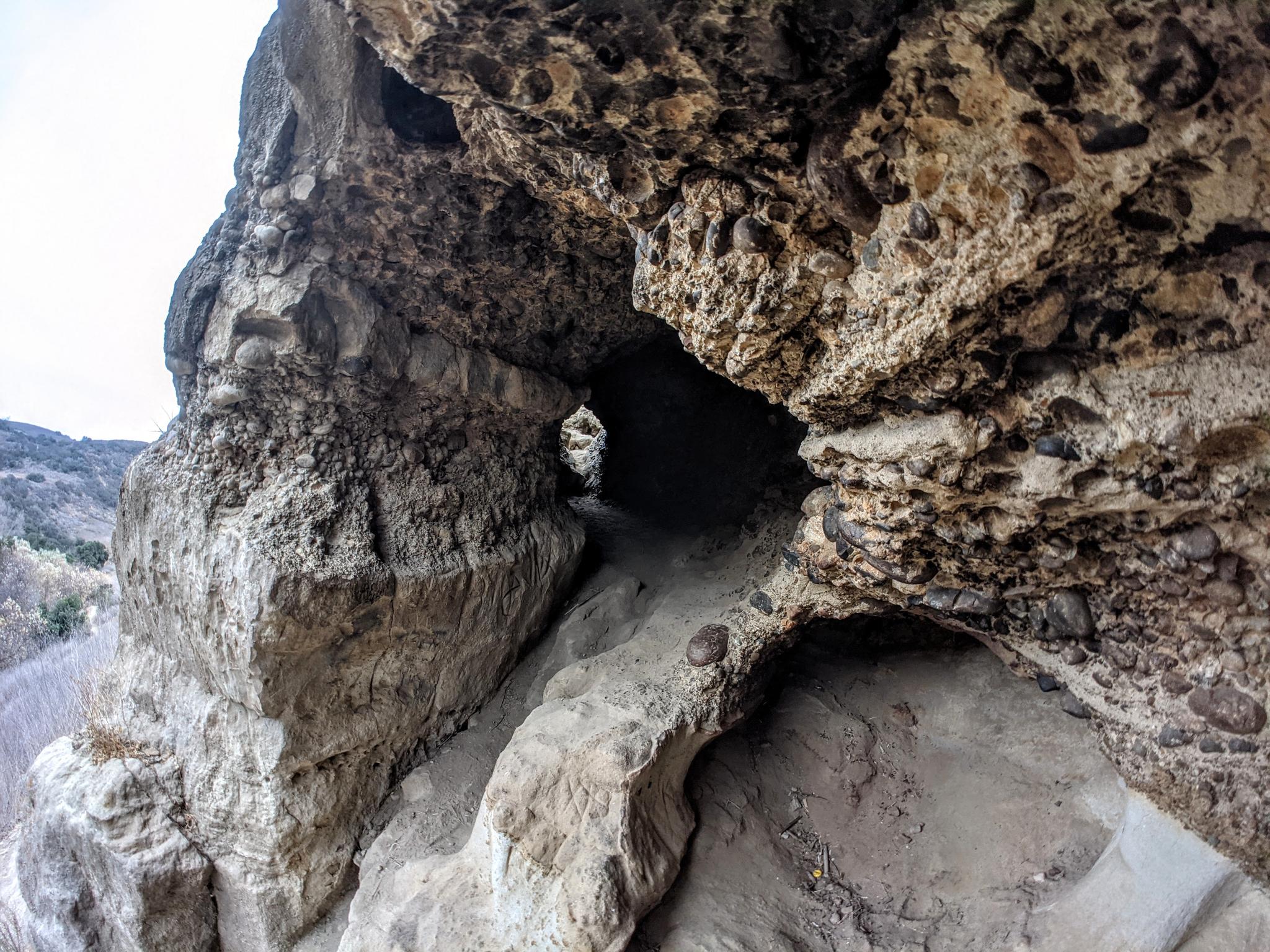 A narrow, dark cave entrance with rough, textured rock walls and a path.