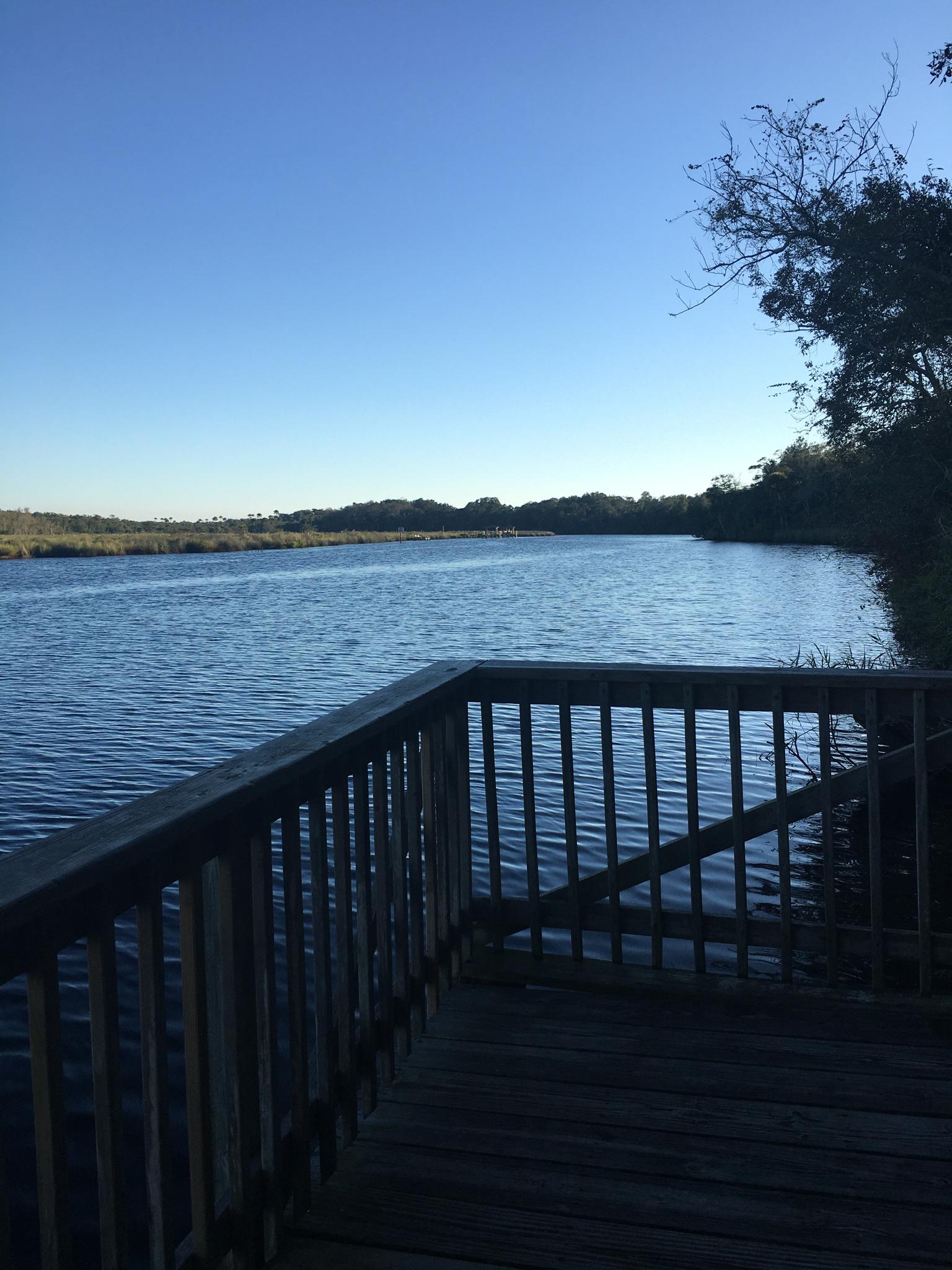 Wooden deck overlooking a calm river under a clear blue sky.
