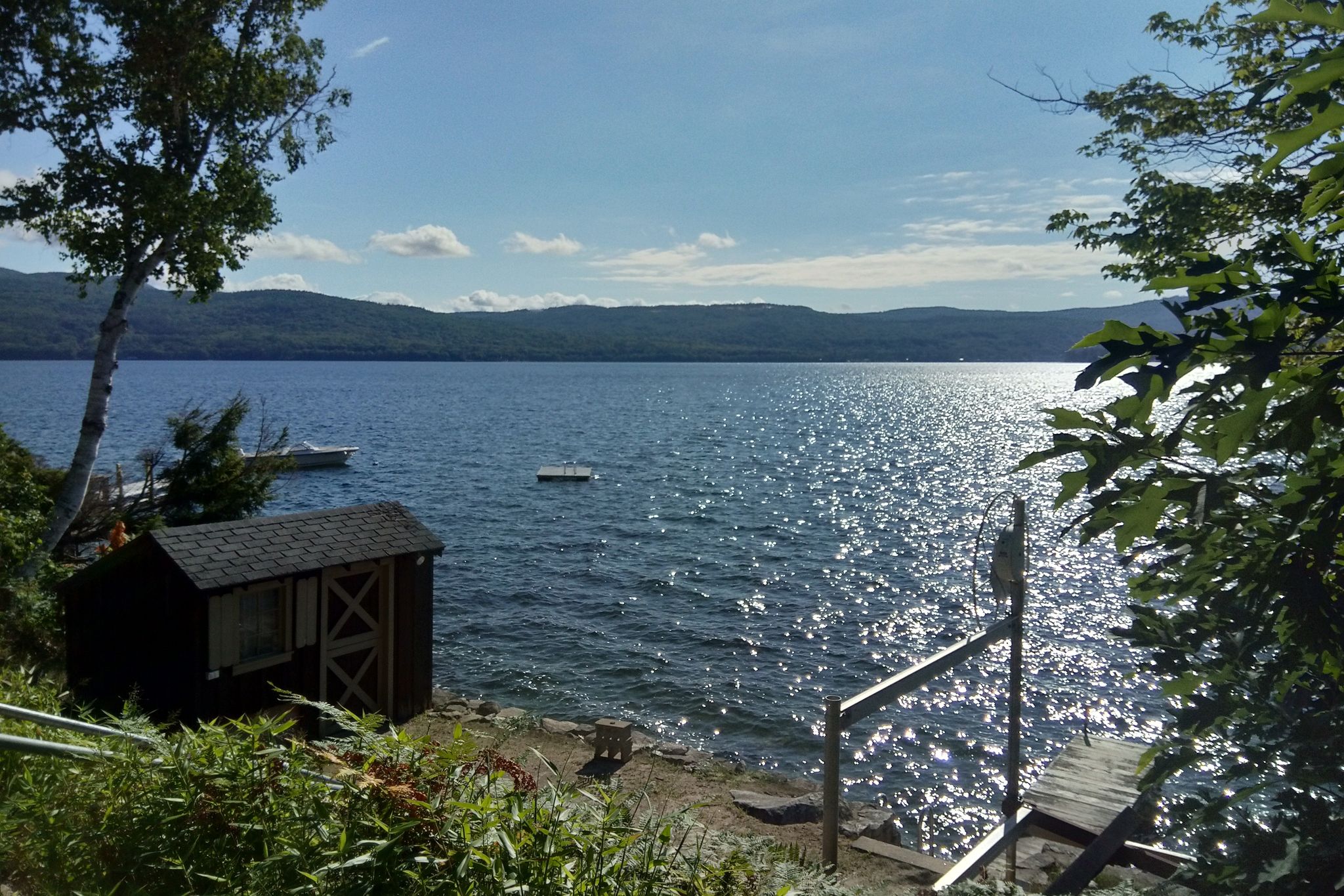 Sunny lake with sparkling water, a small shed, and distant mountains. - Newfound Lake loop from Groton via West Shore Road