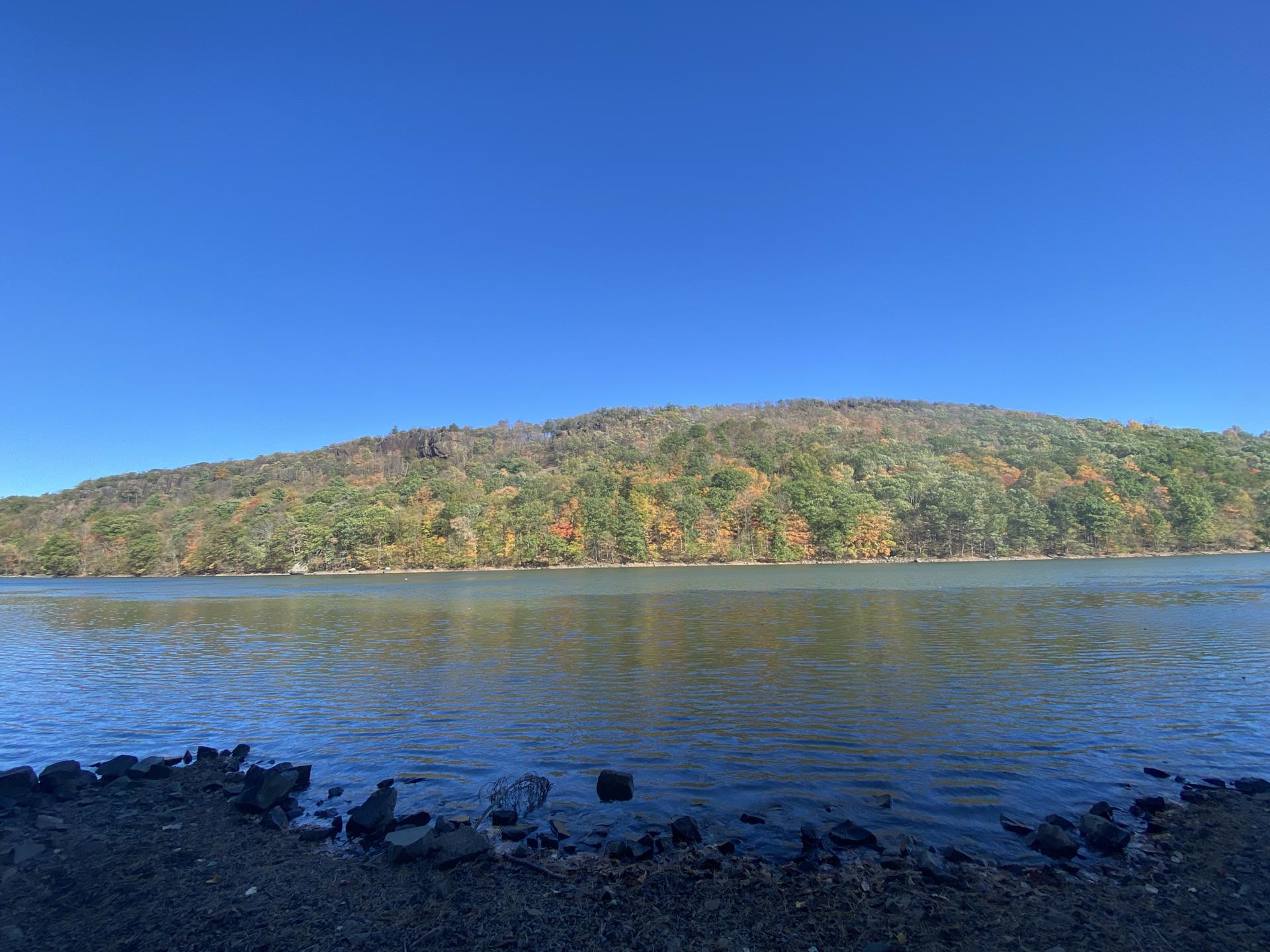 Wide lake with a distant hill showing vibrant autumn foliage under a clear sky.