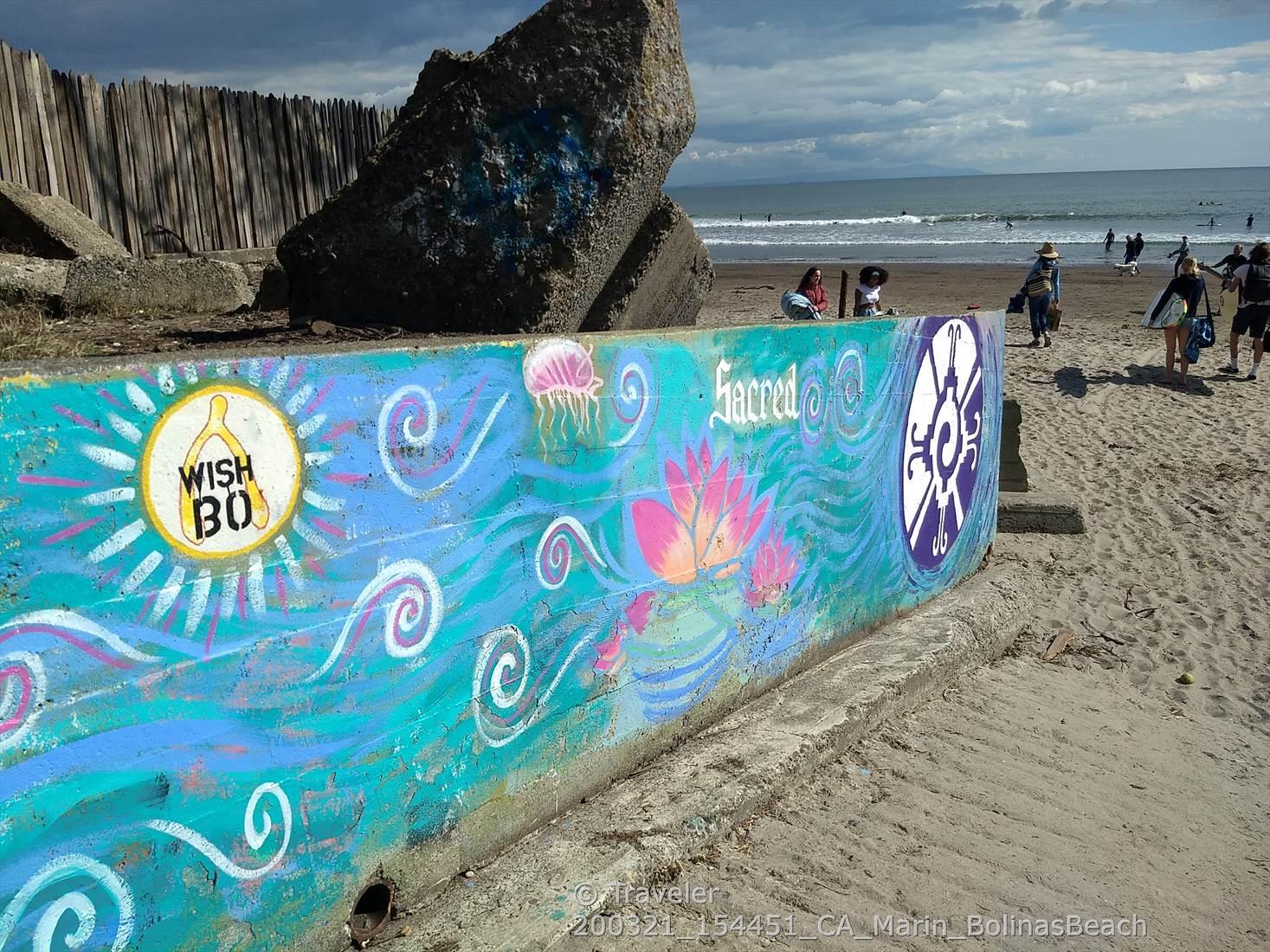 Colorful painted concrete barrier on a sandy beach with people in the distance.
