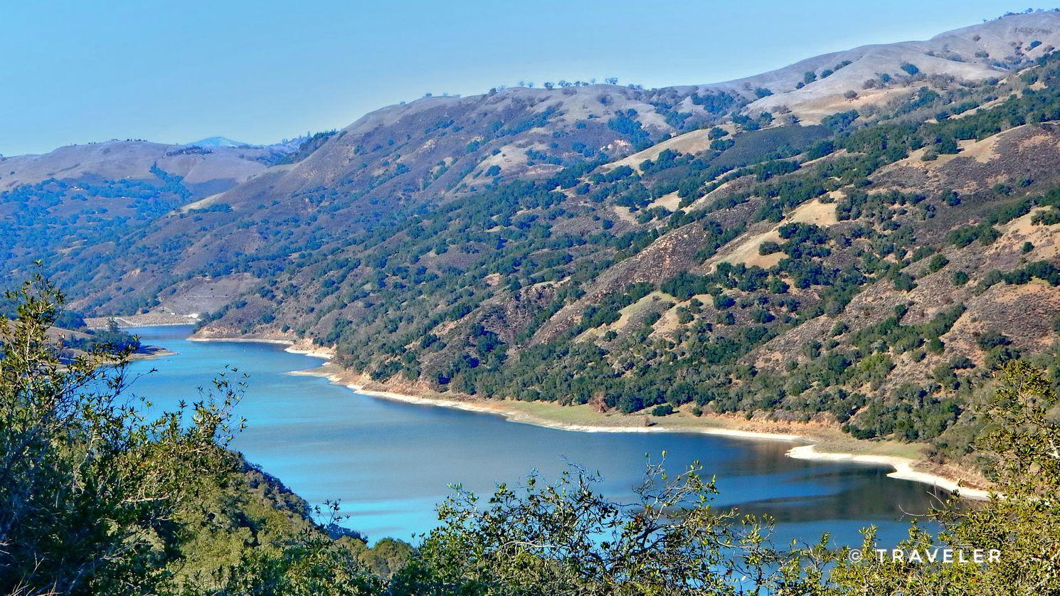 A winding blue lake nestled between tree-covered mountains on a clear day.