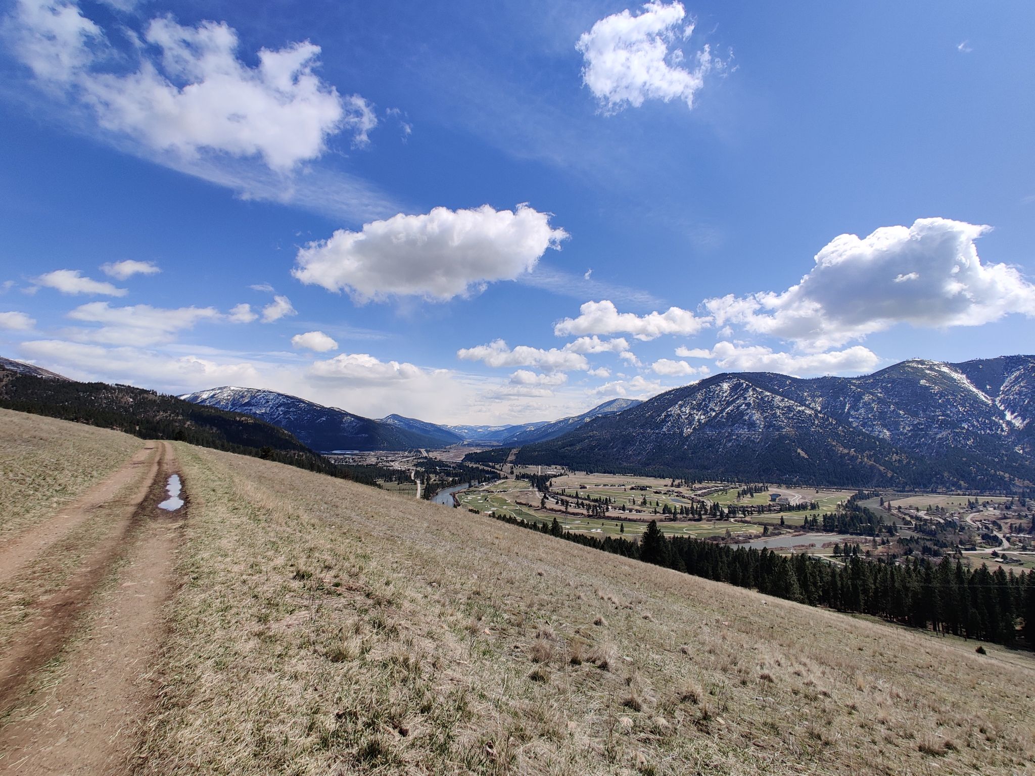 A dirt path on a grassy hill overlooking a wide valley and snowy mountains. - Mount Jumbo Wildlife Management Area loop via Marshall Grade