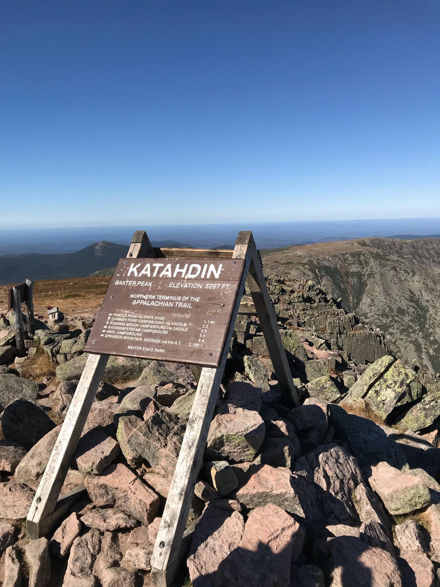 Wooden sign on a rocky mountain peak under a clear blue sky.