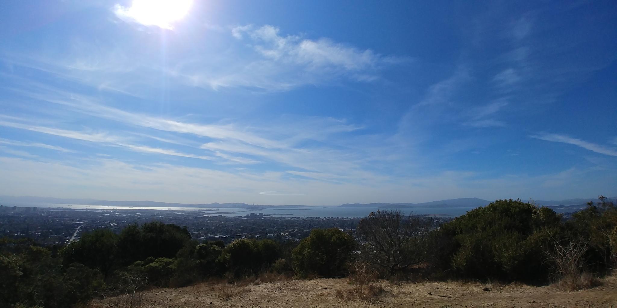 Sunny panoramic view of a distant city and water from a dry hilltop.
