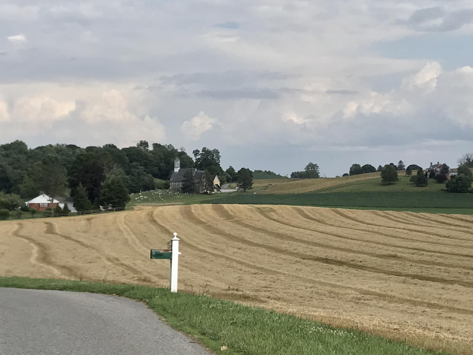 Rural landscape with harvested fields, distant church, and cloudy sky.