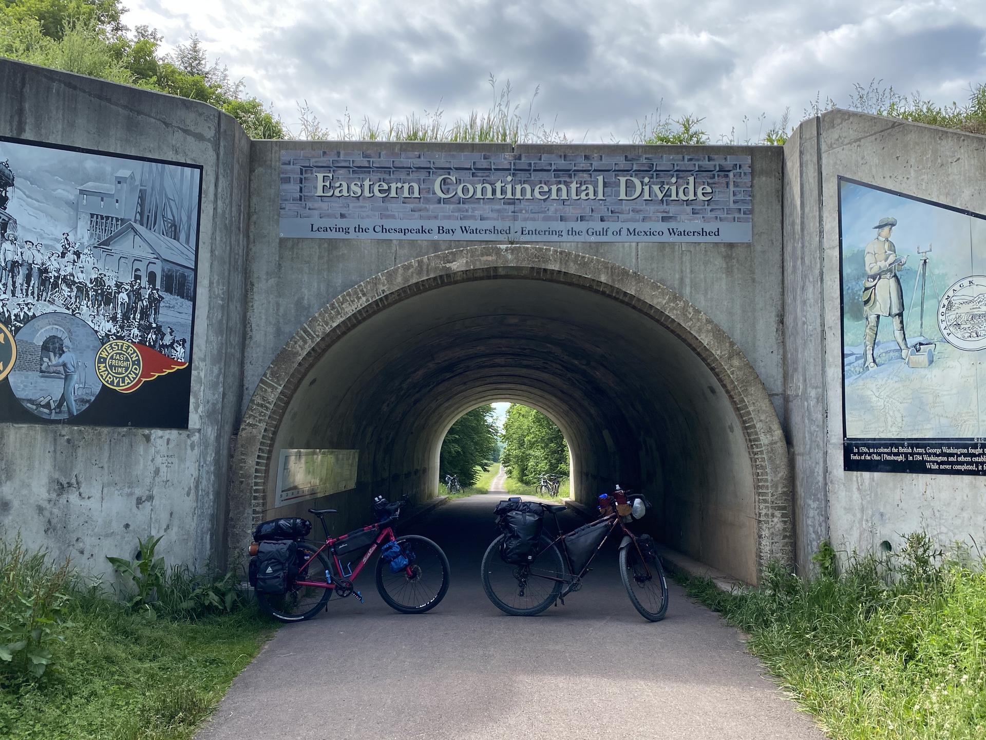 Two bicycles parked before a tunnel entrance with murals under cloudy skies.