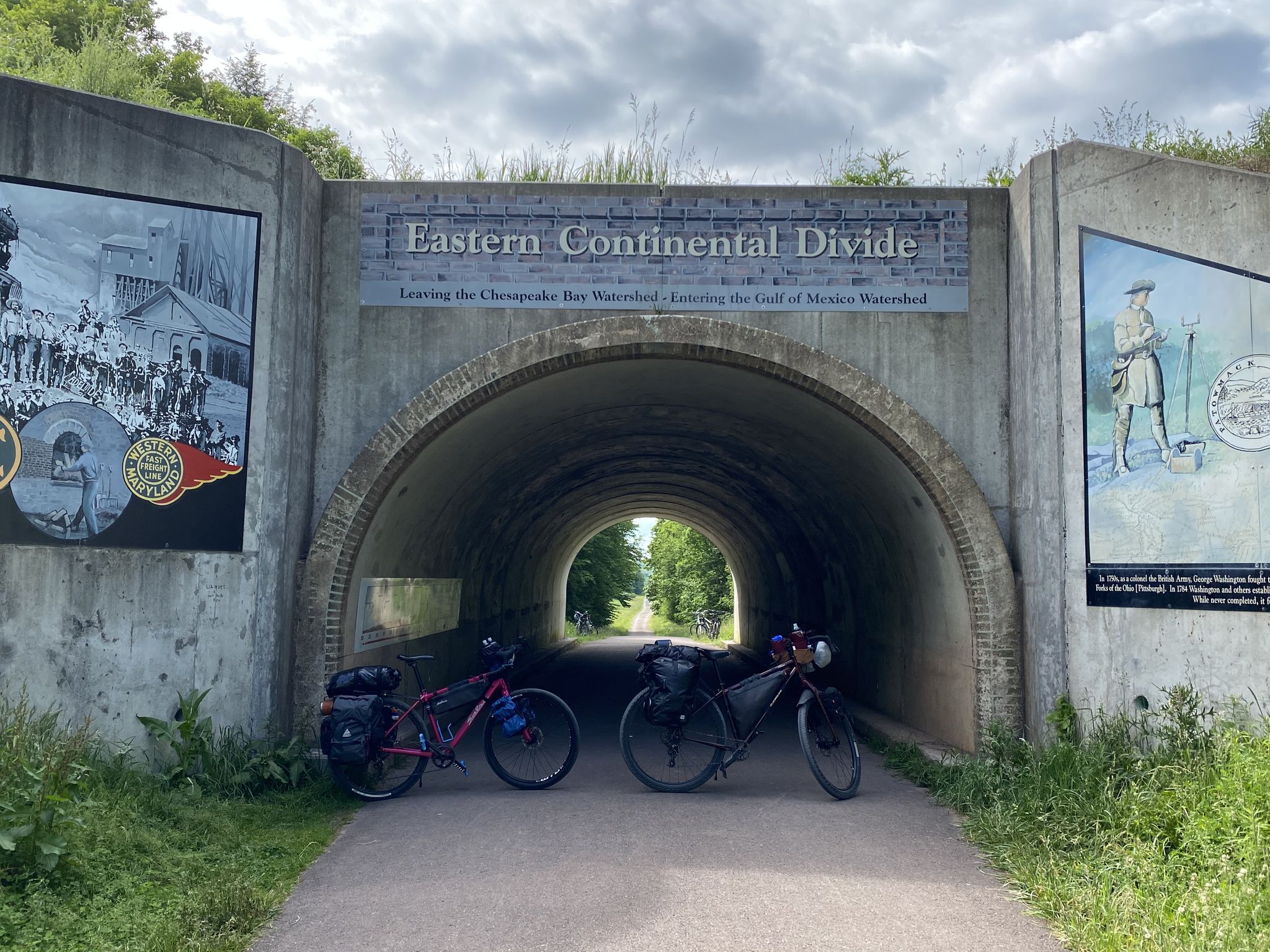 Two bicycles parked before a tunnel entrance with murals under cloudy skies. - Mason-Dixon Line Monument – Big Savage Tunnel loop from Saint Mary Catholic Church