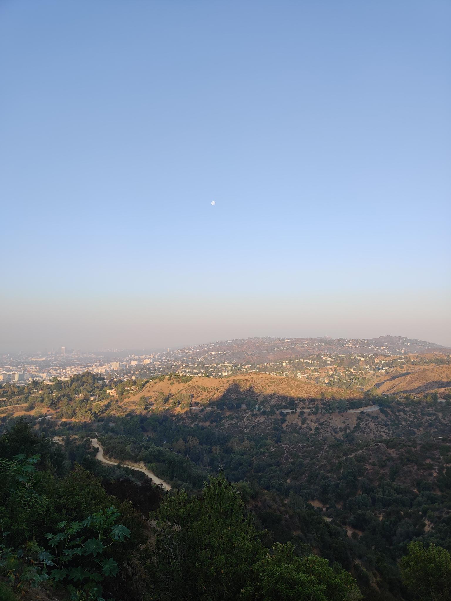 Panoramic view of a city nestled among hills under a clear sky.