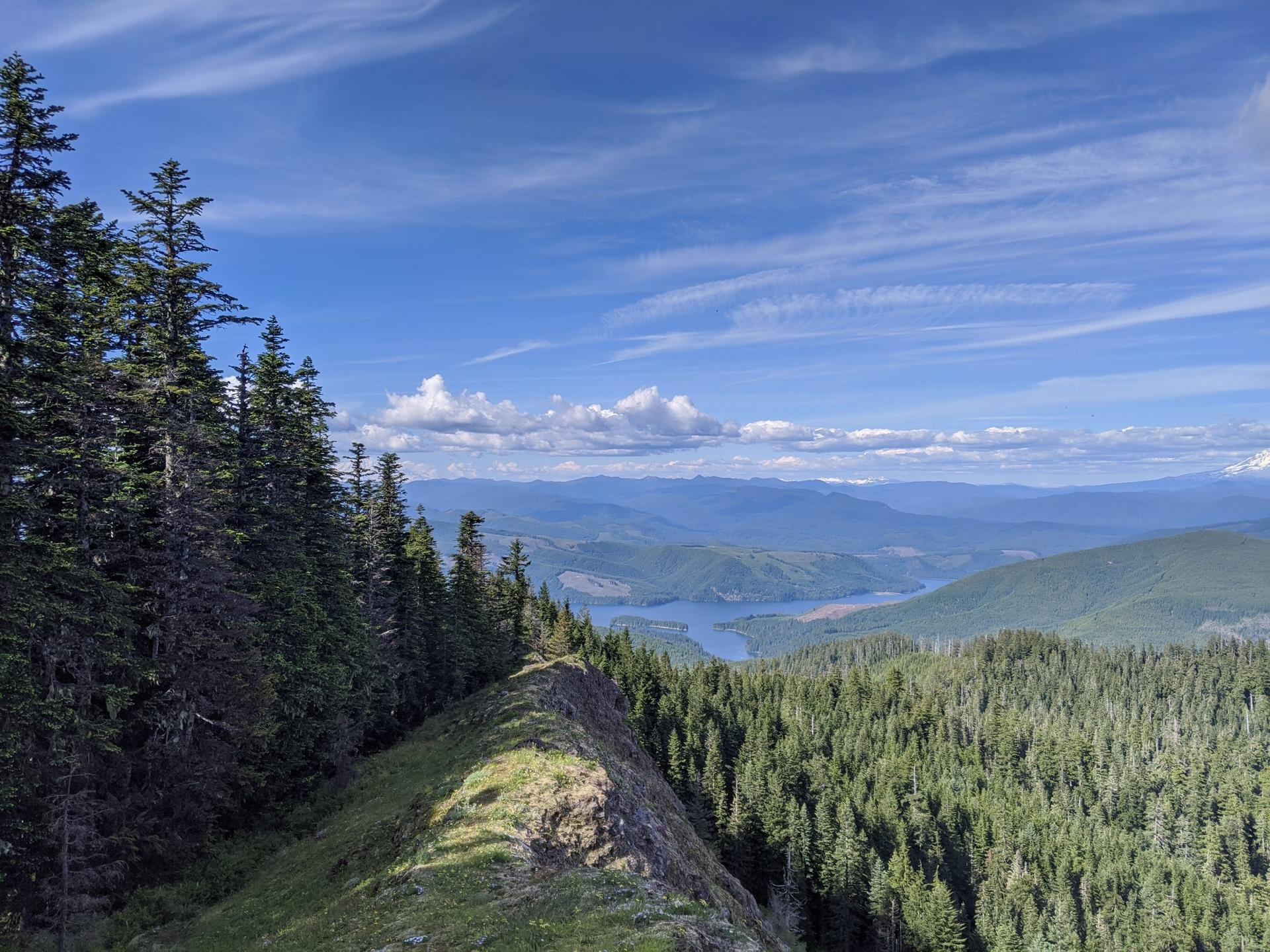 View from a mountain ridge overlooking a vast forest and distant lake.