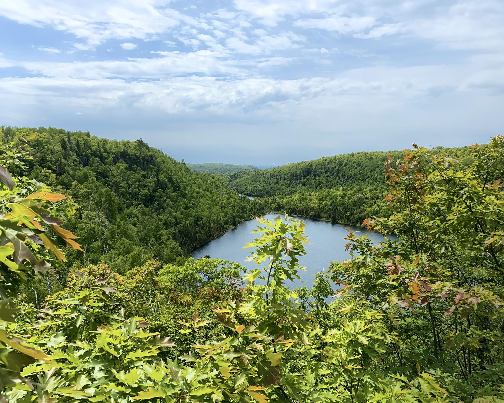 Lake nestled in dense green forest under a partly cloudy sky, seen from above.