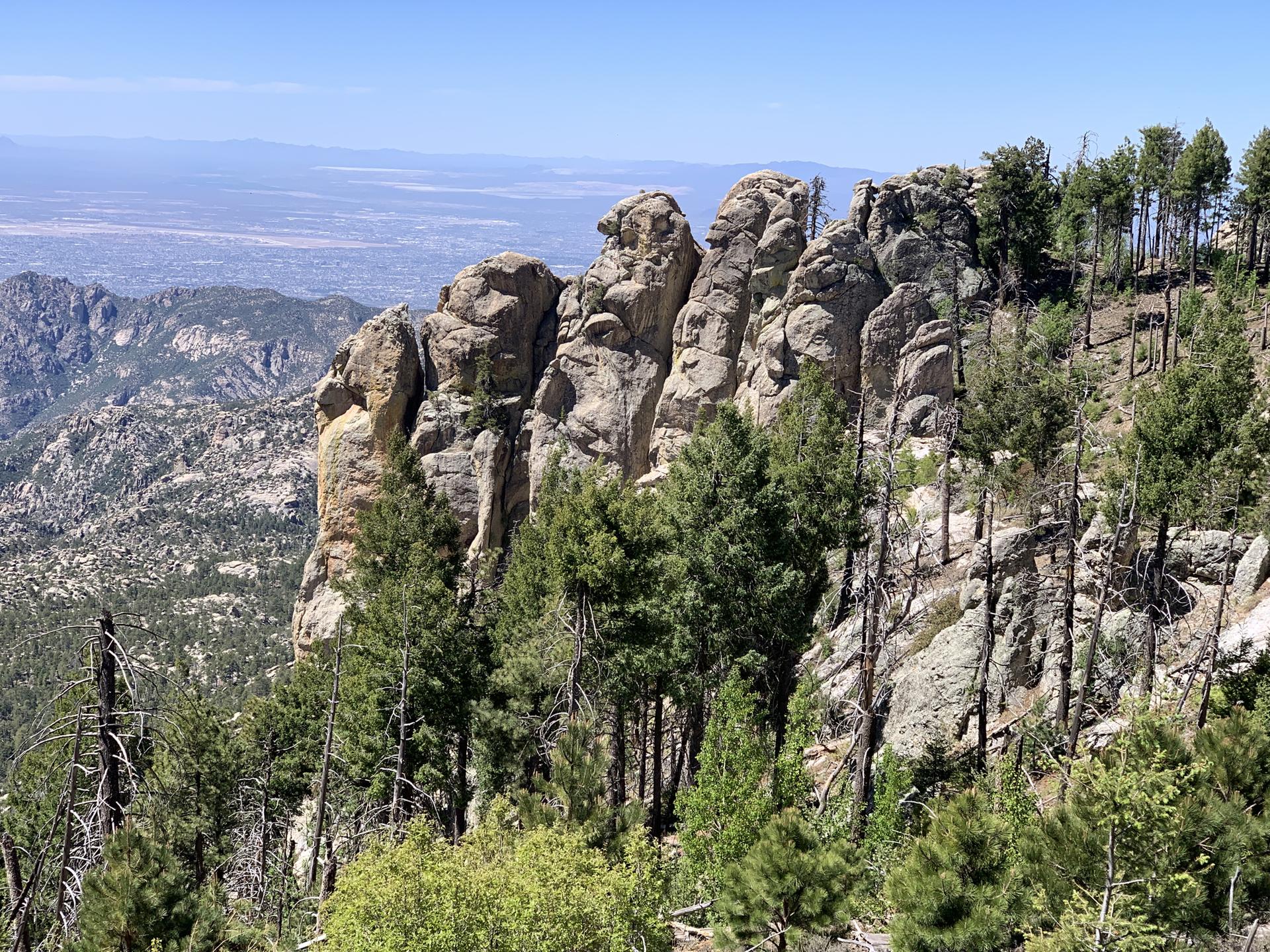 Towering rock formations and pine trees on a mountain ridge overlooking a valley.