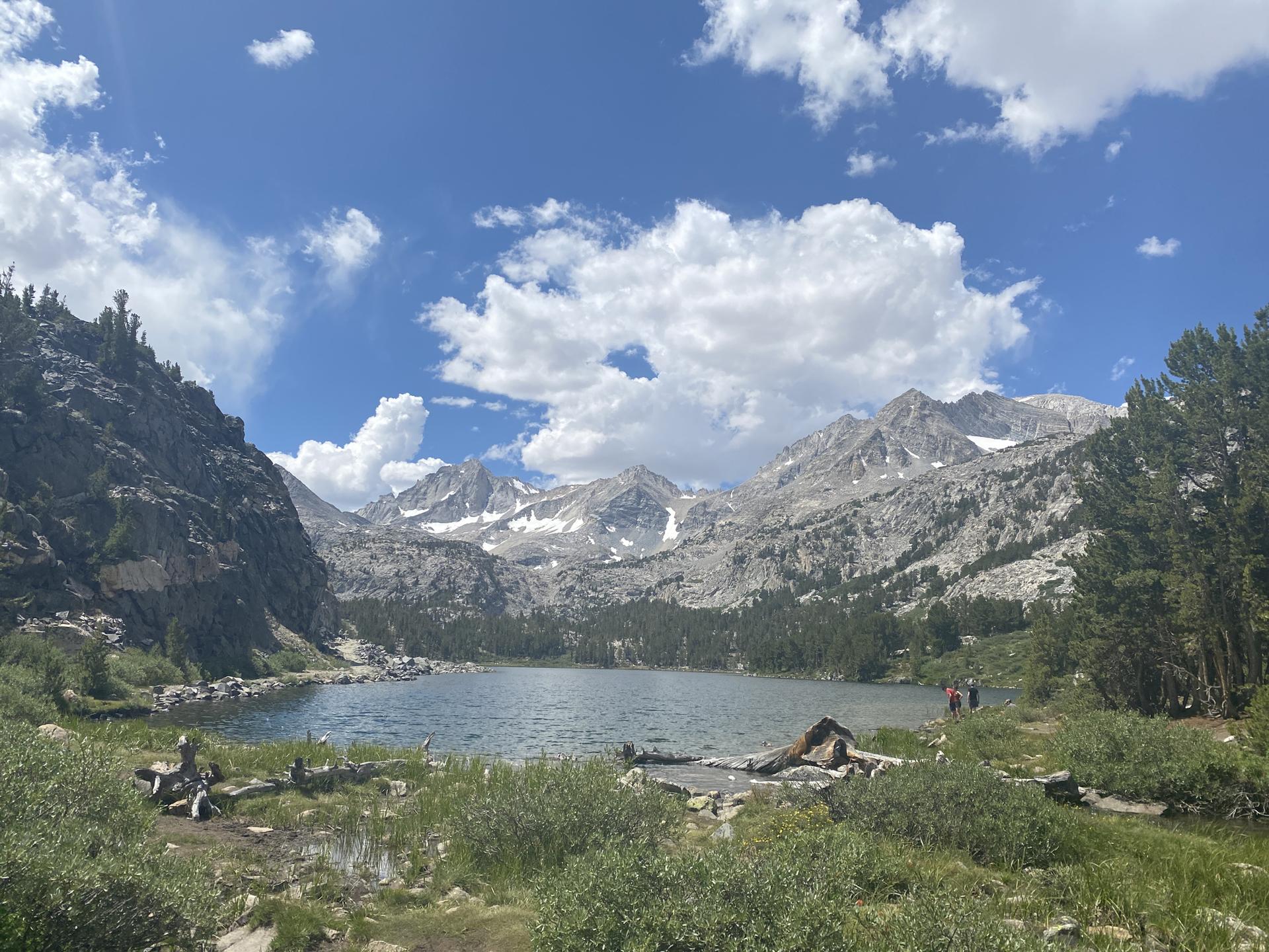 A wide lake surrounded by rocky mountains and green forests under a cloudy sky.