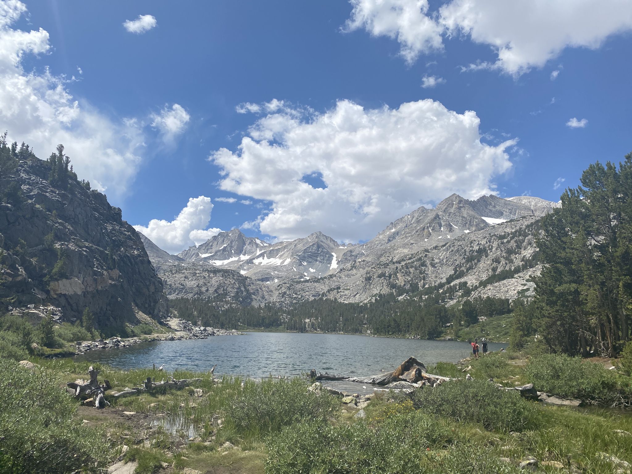 A wide lake surrounded by rocky mountains and green forests under a cloudy sky. - Little Lakes Valley Trail