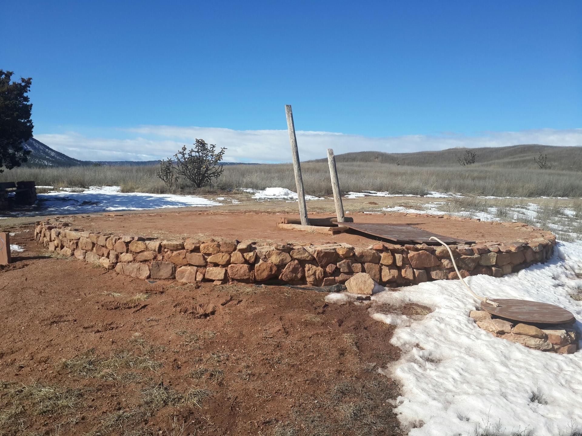 Circular stone structure with wooden posts in a snowy, arid landscape.