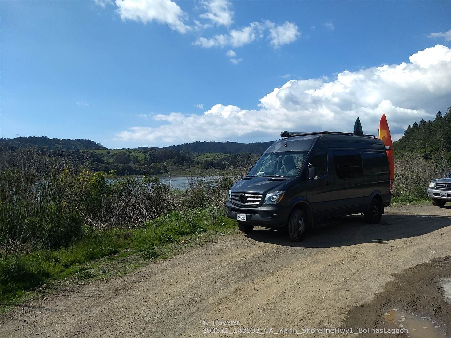 Black van with surfboards parked on a dirt road by a lake. - Martin Griffin Preserve – Bolinas Wharf loop from Stinson Beach