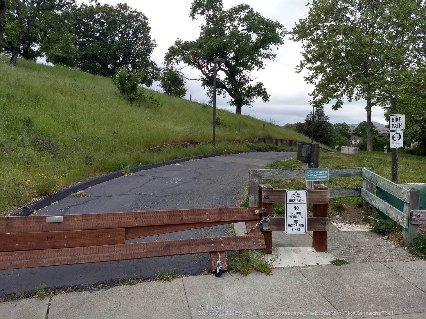 A wooden gate blocks a paved path next to a grassy hillside. - Running loop from Loma Verde