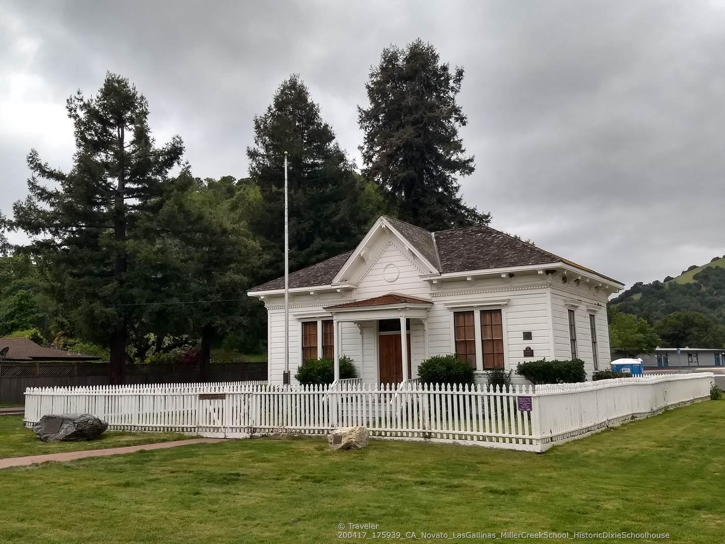 A white house with a picket fence on a green lawn under cloudy skies.