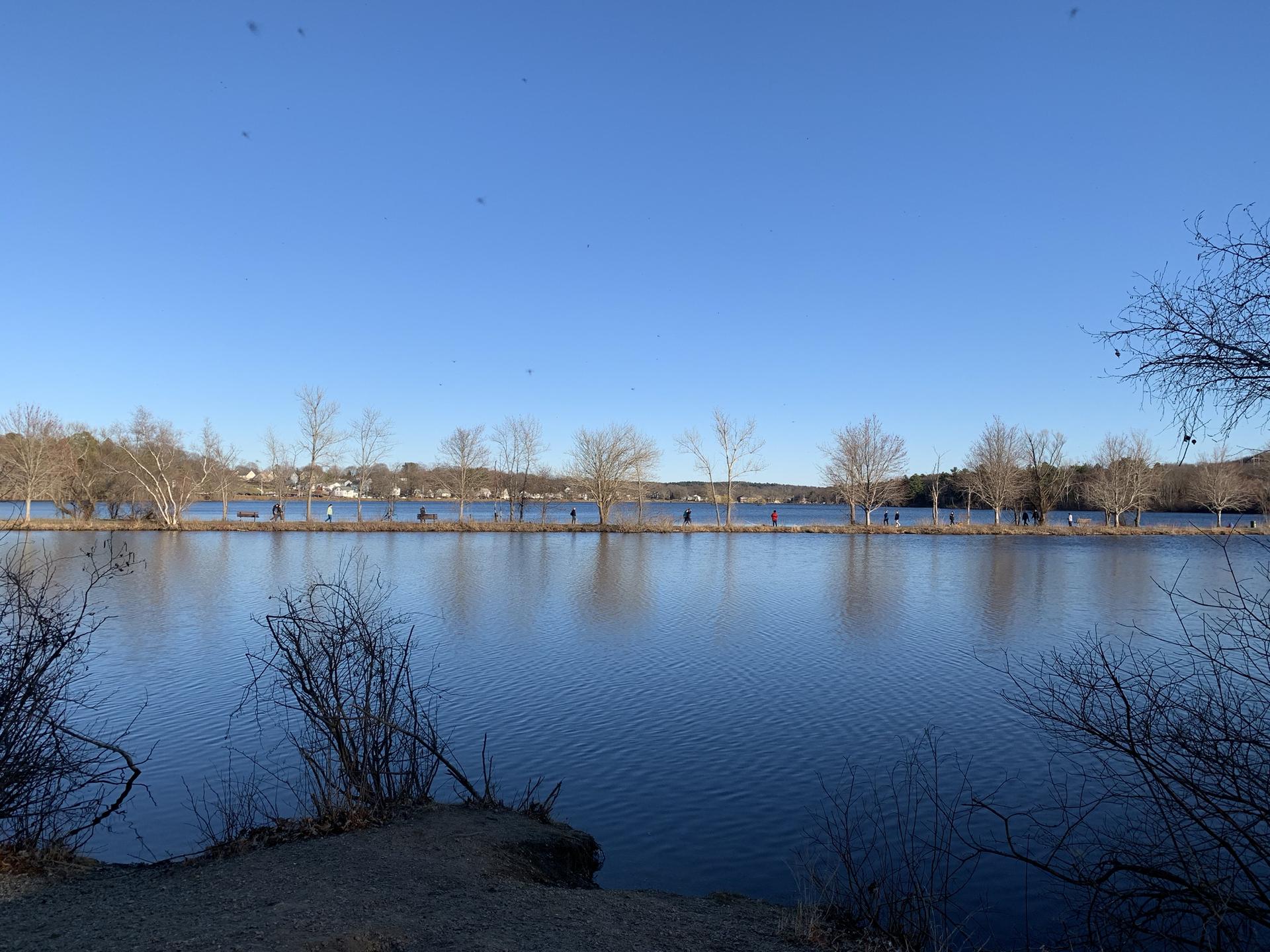 Wide lake under clear blue sky, people walking on distant shore.