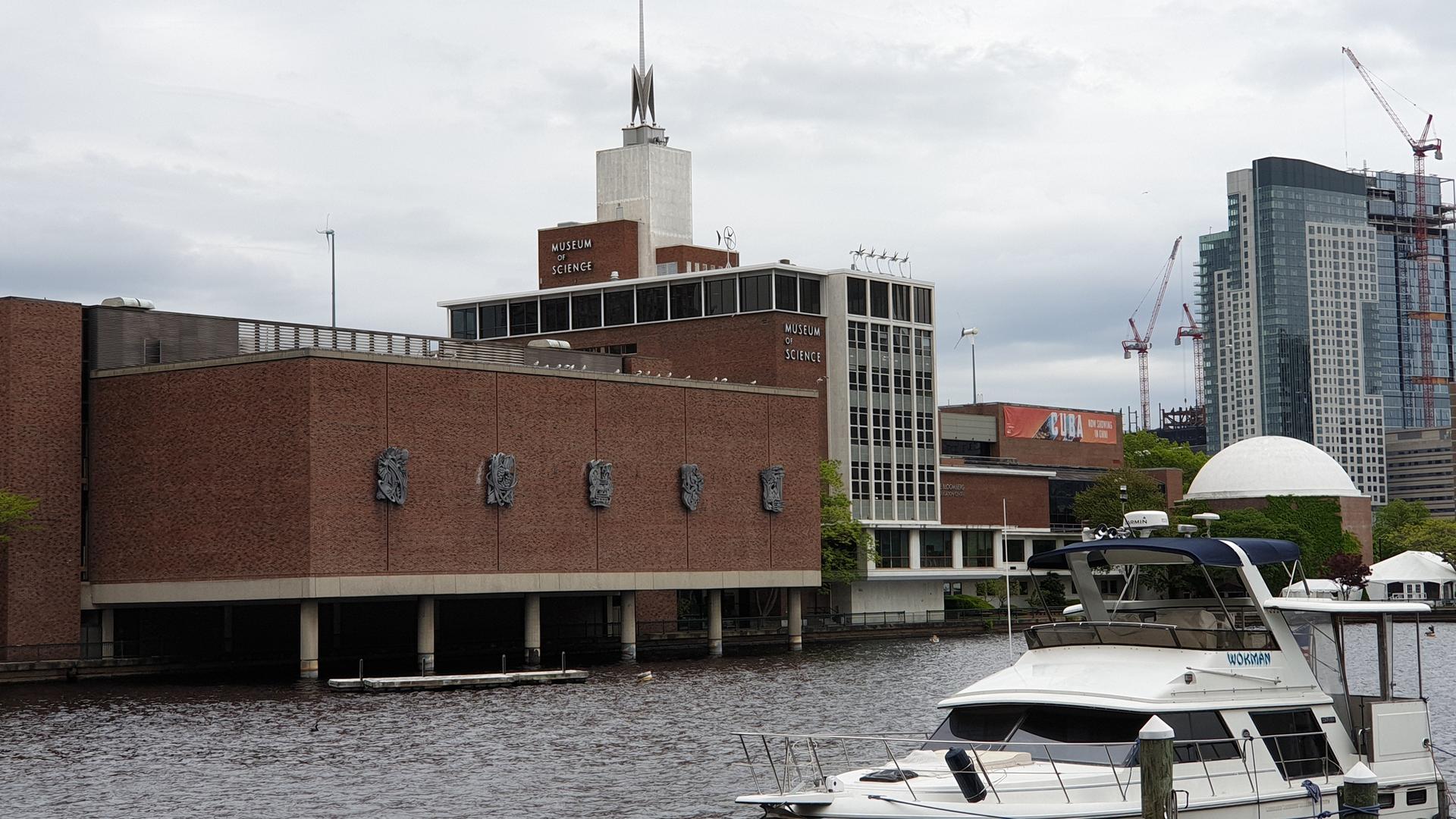 A large brick building by the water with a docked boat and construction cranes.