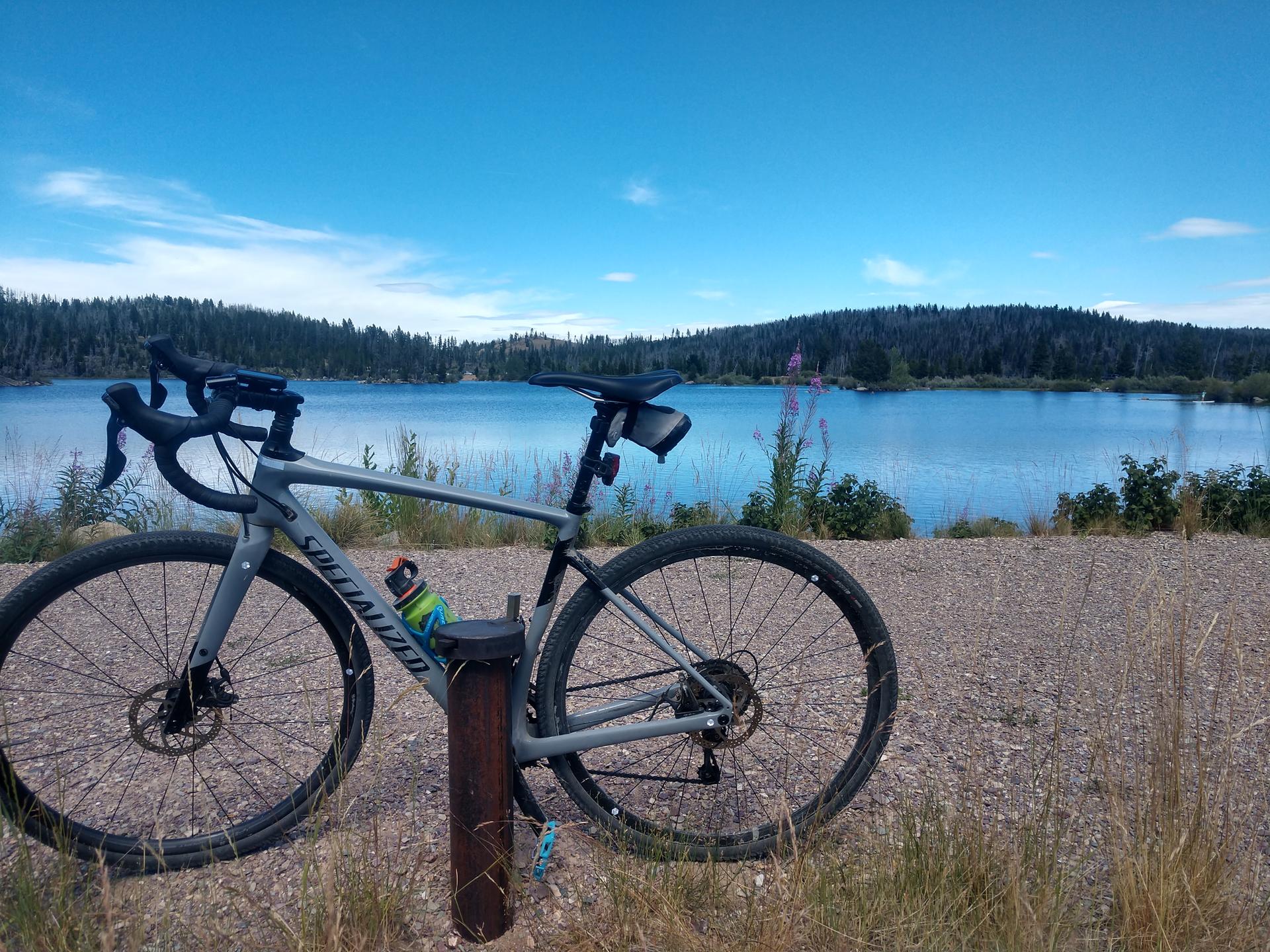 Gray gravel bike parked beside a calm blue lake under a clear sky.