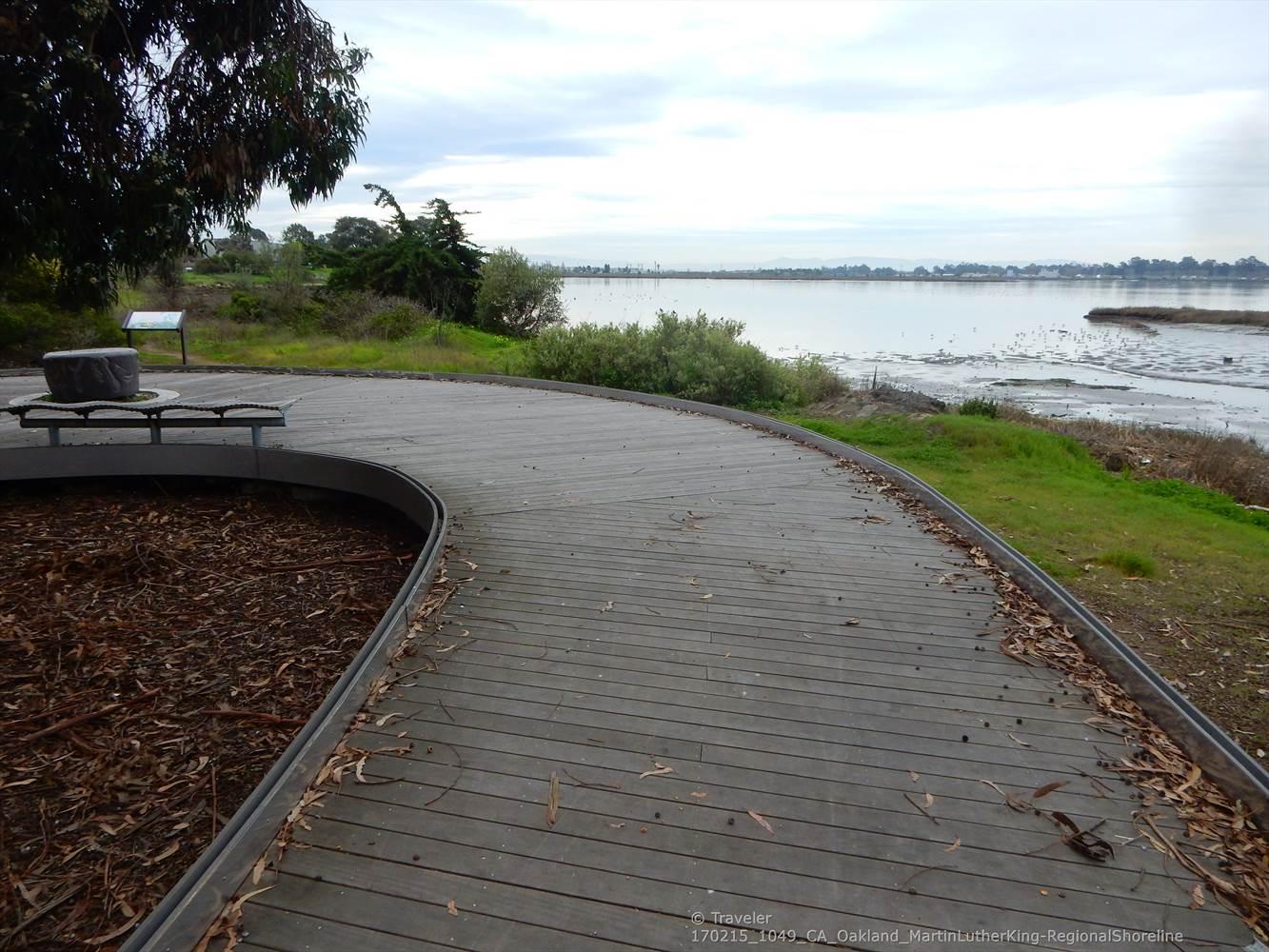 Wooden boardwalk with a bench overlooking a calm body of water.